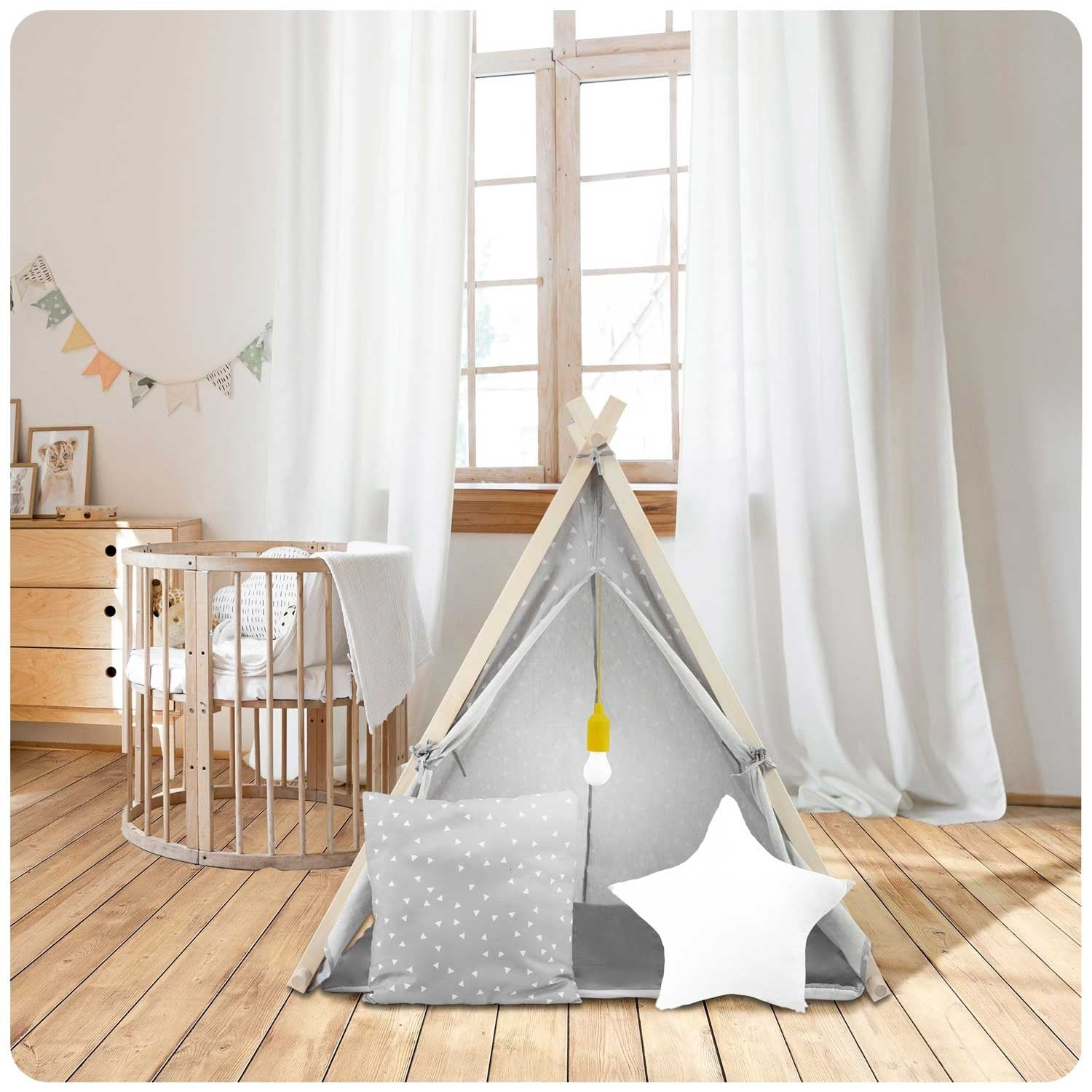Una habitación infantil con tipi, cuna y cojín de estrella. Cortinas blancas, suelo de madera y una guirnalda añaden calidez.