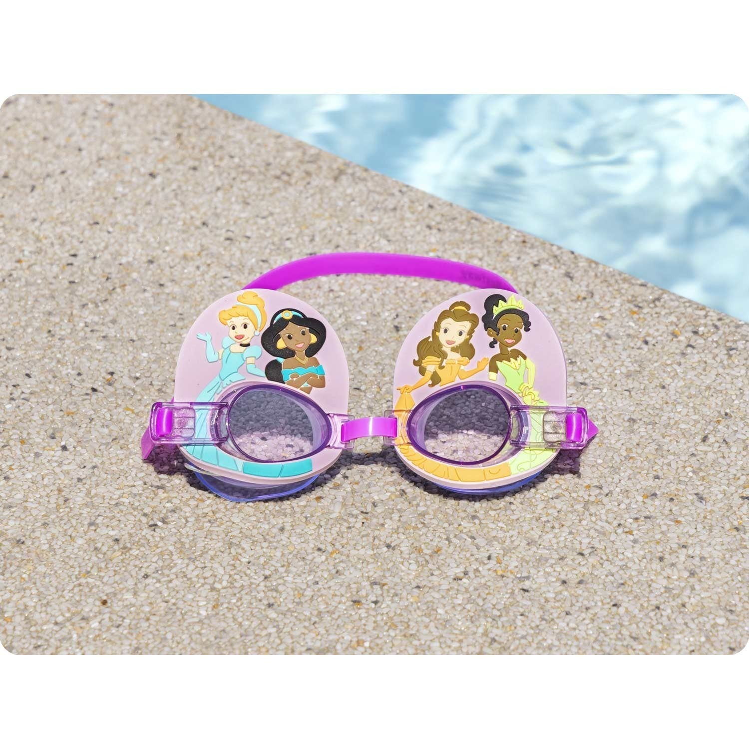 Gafas de natación rosas con princesas Disney. Descansan sobre una superficie texturizada, con agua de piscina al fondo.