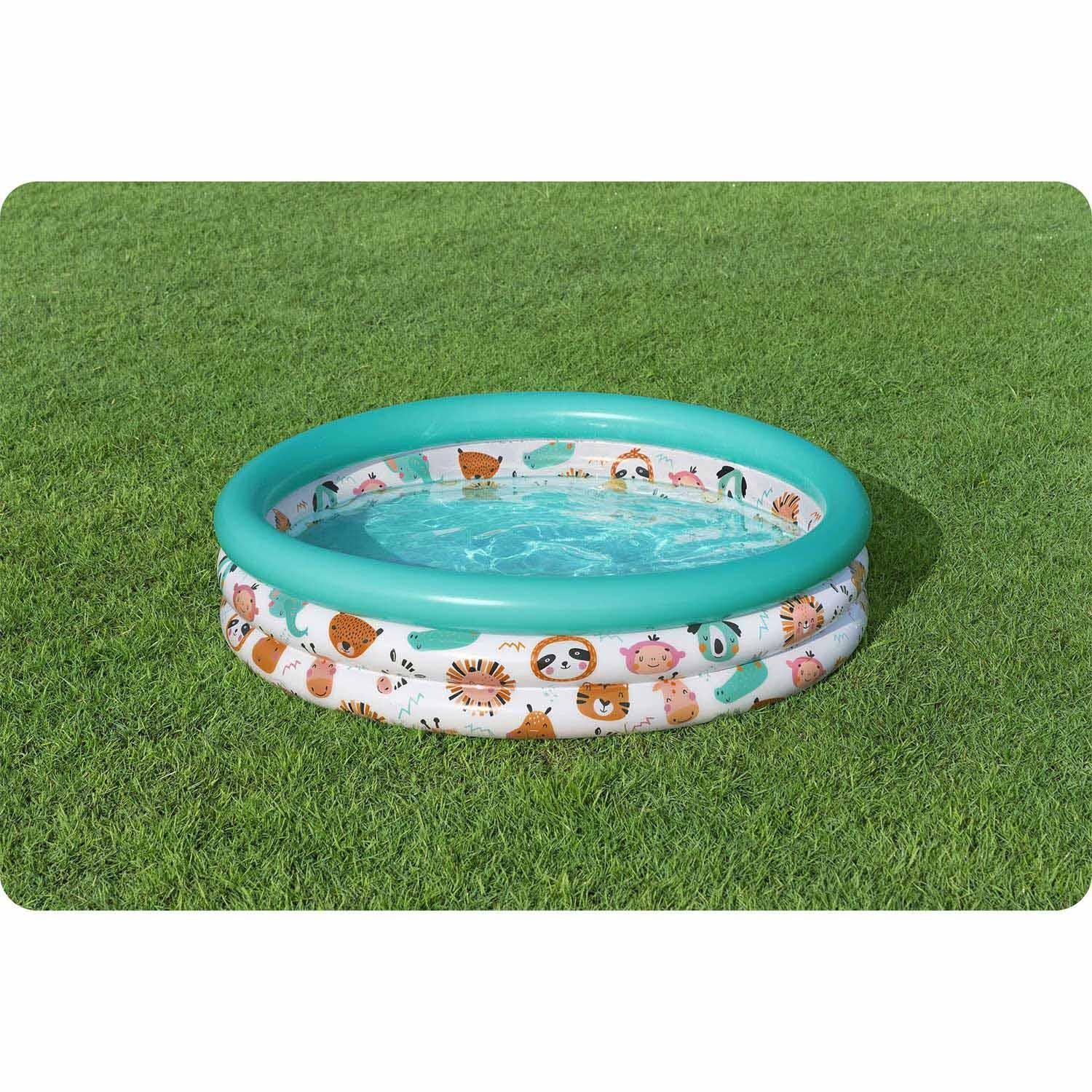 Una pequeña piscina inflable redonda sobre hierba verde. La piscina es turquesa con una base blanca decorada con patrones de animales.