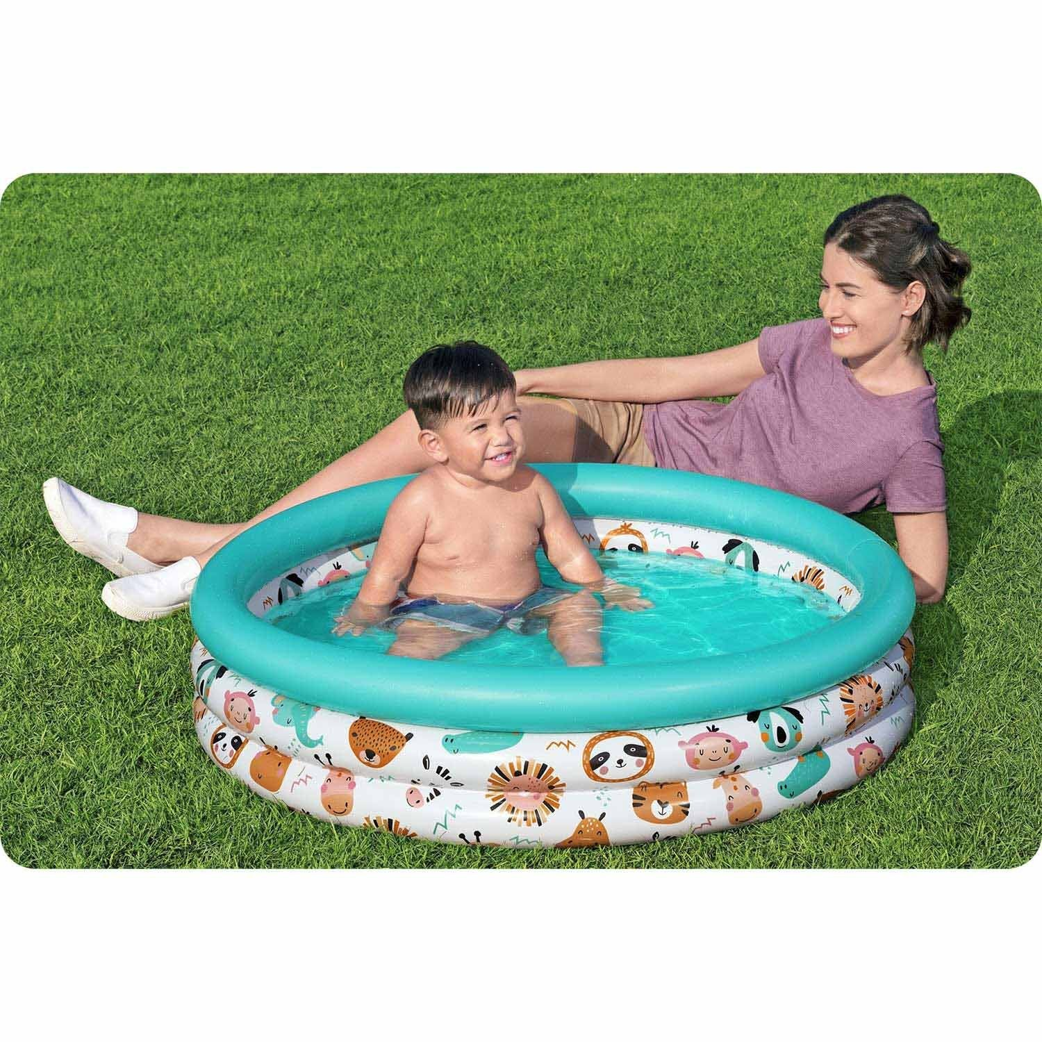 Un niño está en una piscina con una mujer acostada en el césped. La piscina tiene diseños de animales.