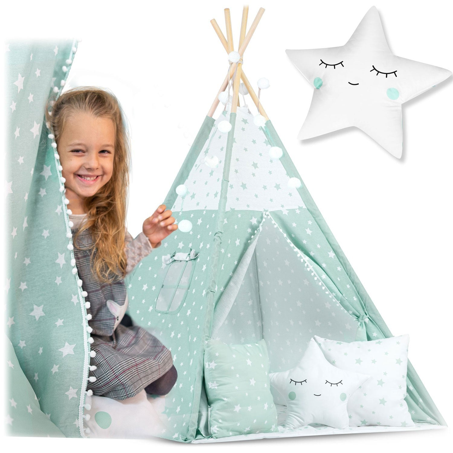 Una niña sonríe, asomándose desde una tienda de campaña con estampado de estrellas. Una almohada en forma de estrella y otras almohadas están cerca.