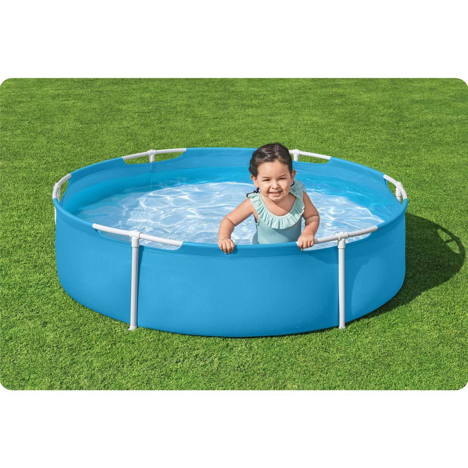 Una niña en un traje de baño azul sonríe en una piscina inflable azul y redonda. Está sobre césped verde.