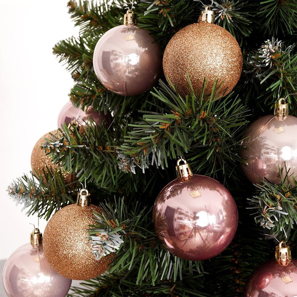 Primer plano de un árbol de Navidad decorado. Adornos oro rosa y brillantes cuelgan de ramas verdes sobre un fondo blanco.