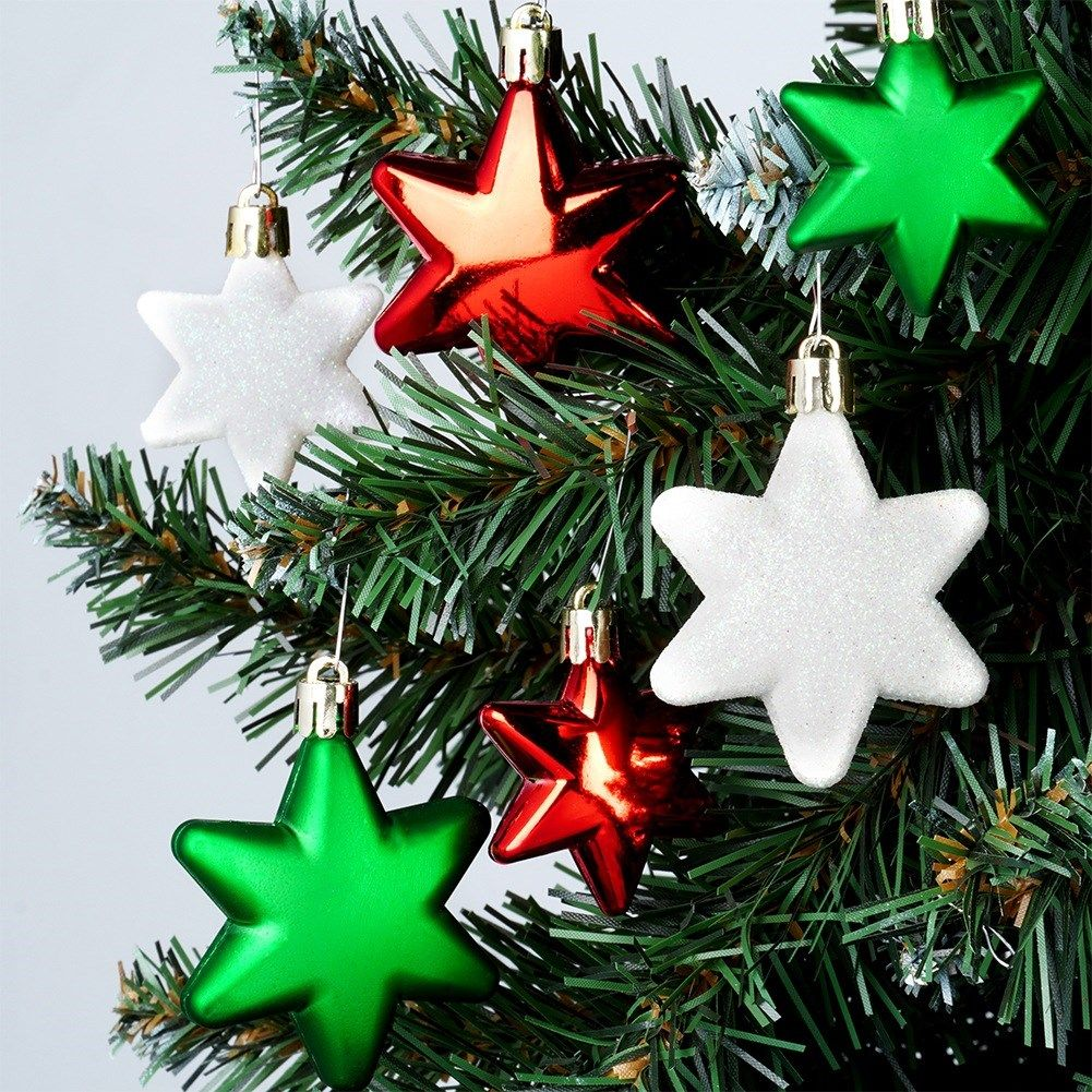 Primer plano del árbol de Navidad con adornos. Estrellas rojas, verdes y blancas cuelgan de las ramas. El fondo es gris claro.