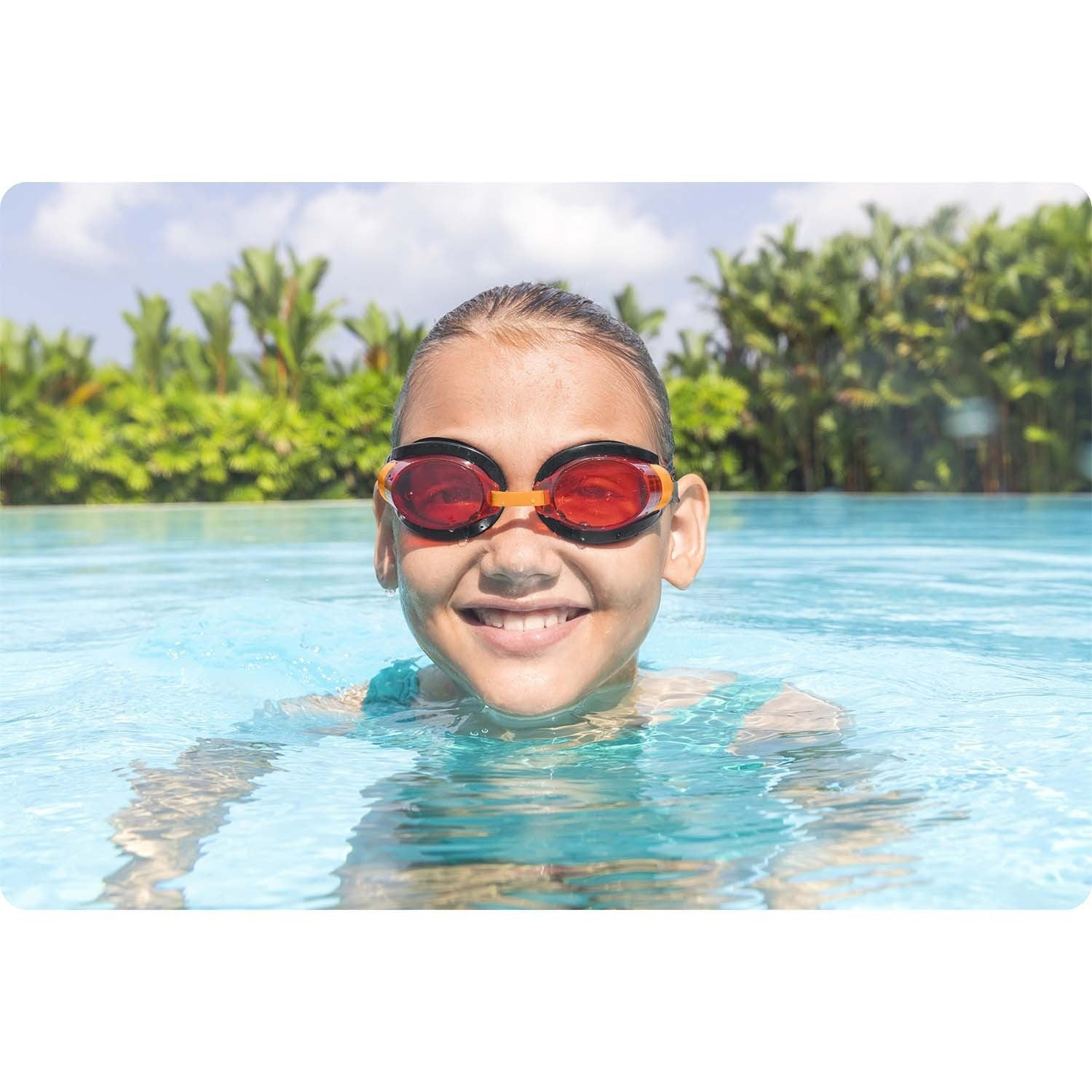 Una niña con gafas sonríe en una piscina. El agua es azul y hay árboles verdes en el fondo bajo un cielo azul.