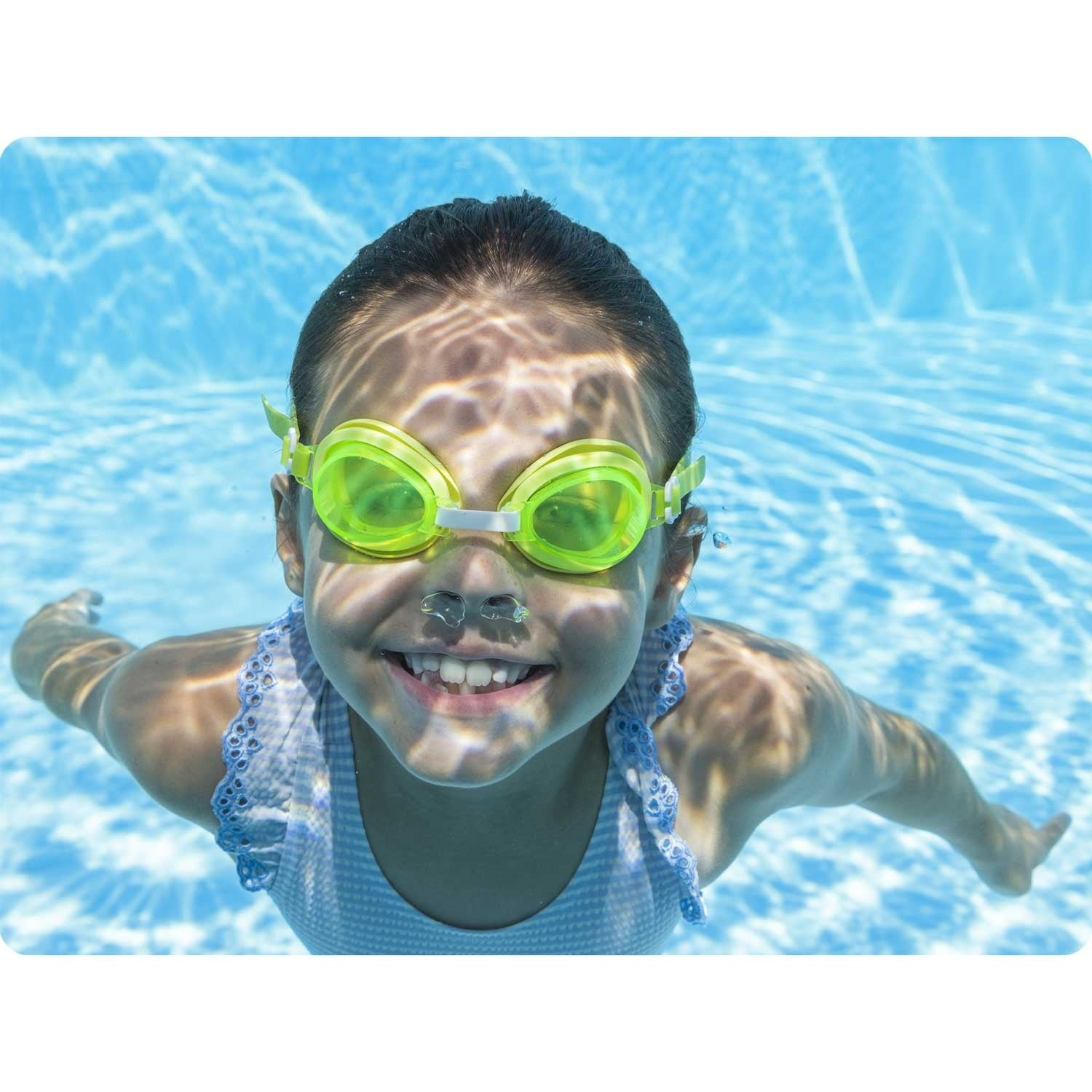 Una niña nada bajo el agua, con gafas amarillas. Sonríe, con los brazos extendidos. El fondo es una piscina azul con reflejos solares.