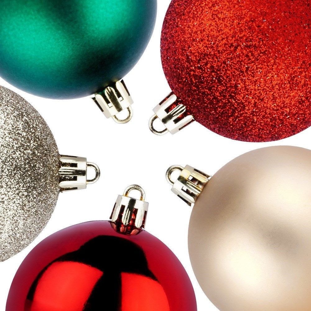 Primer plano de cinco adornos navideños en rojo, verde, dorado y plateado. Están dispuestos sobre un fondo blanco.
