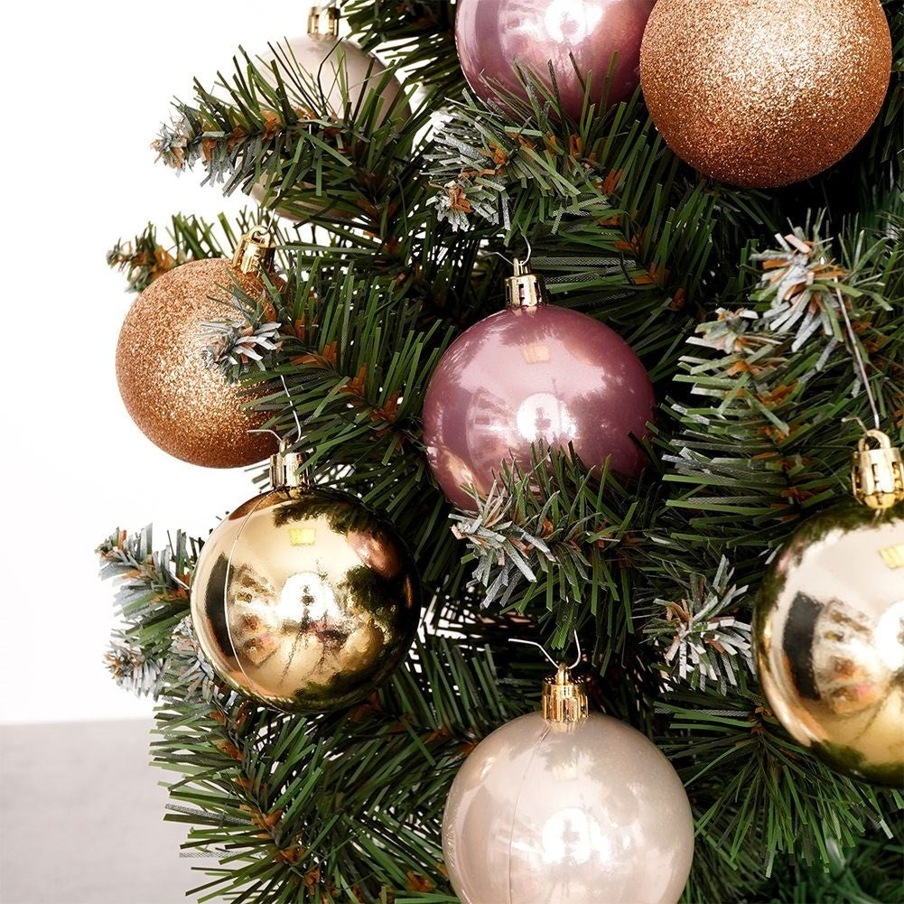 Primer plano de un árbol de Navidad decorado con adornos dorados, rosas y plateados. Se ven agujas verdes y fondo blanco.