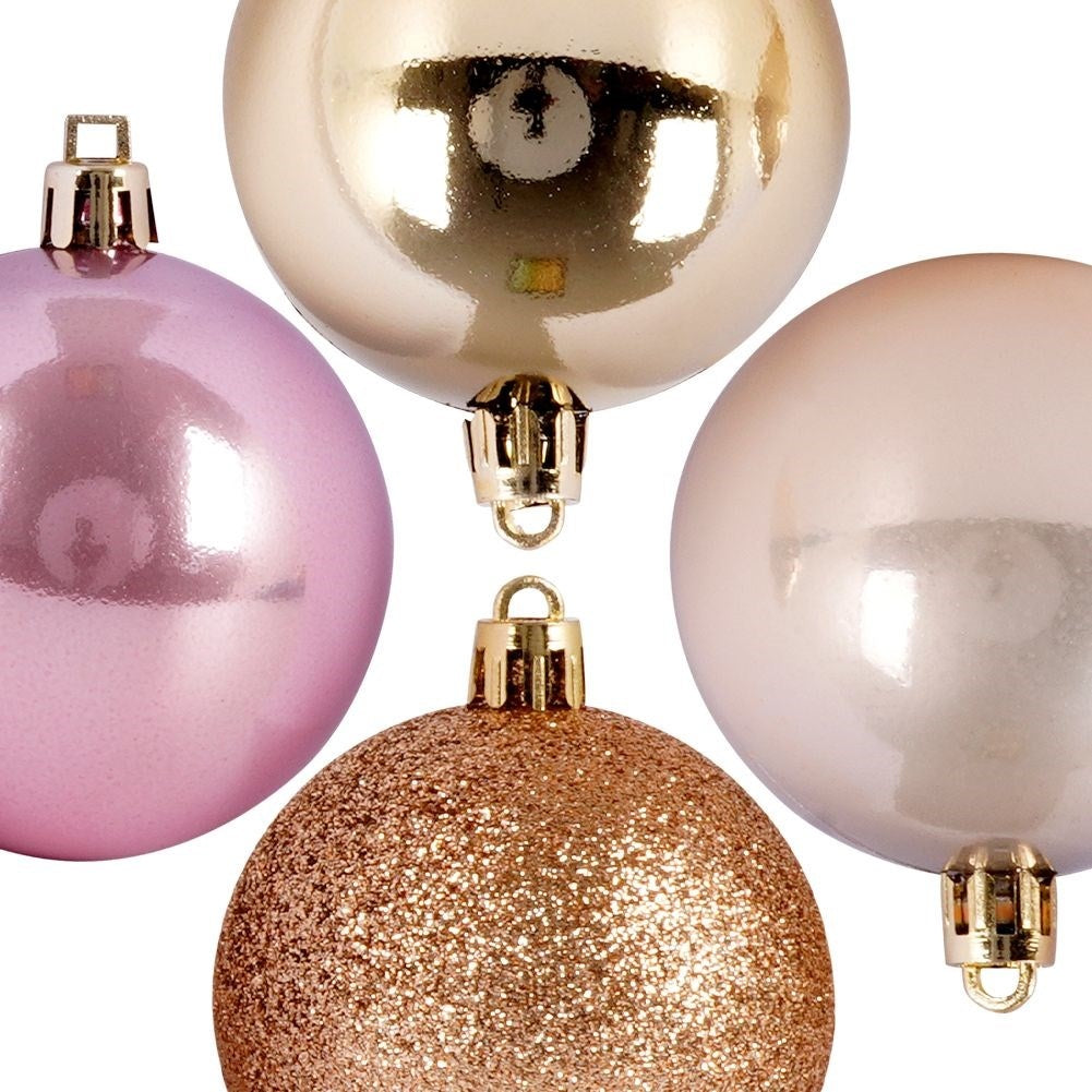 Cuatro adornos navideños coloridos. Rosa, dorado, rosa claro y dorado brillante, cada uno con una tapa dorada, sobre fondo blanco.