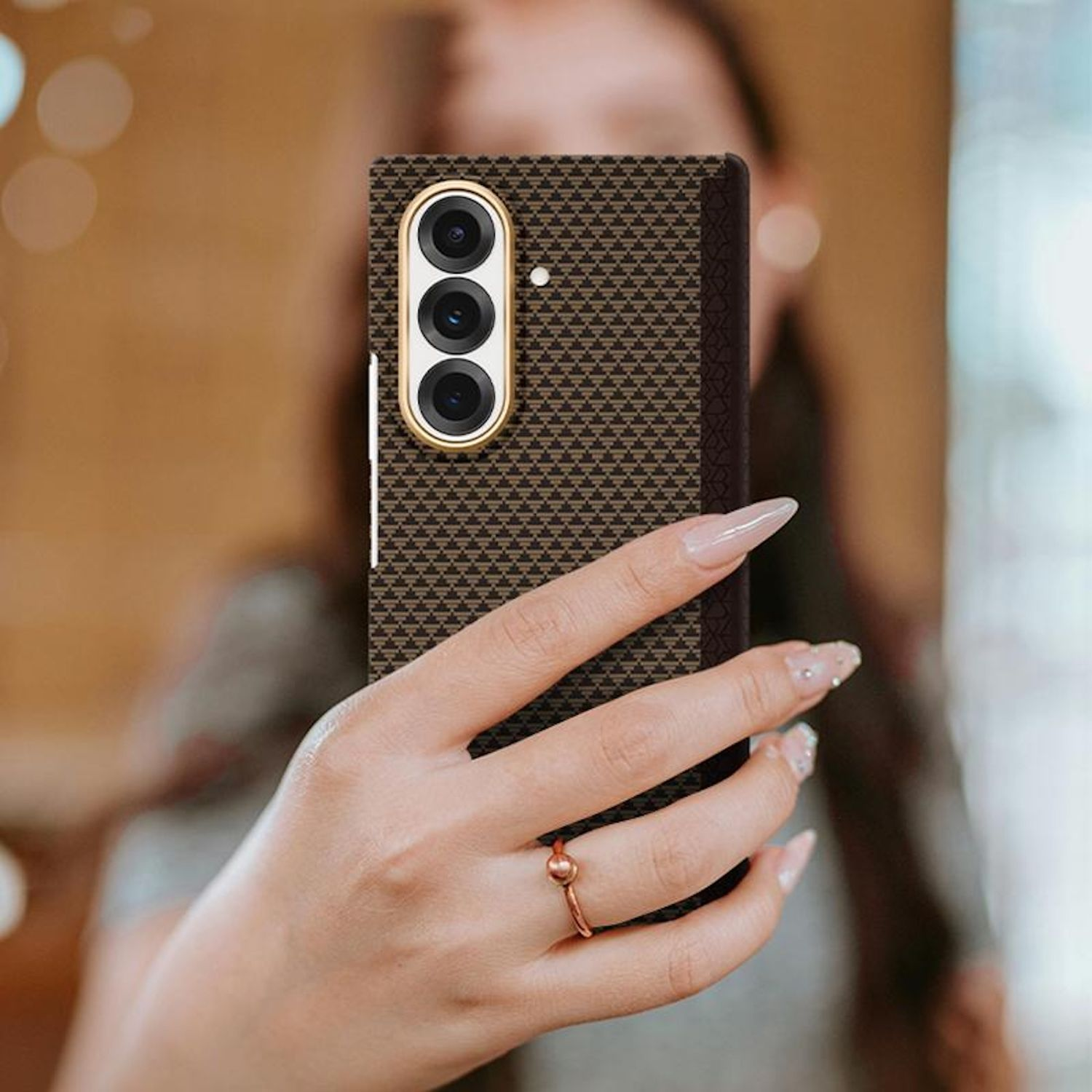 Una persona sosteniendo un teléfono estampado. El teléfono tiene tres cámaras y un marco dorado. La persona usa un anillo y tiene uñas largas.