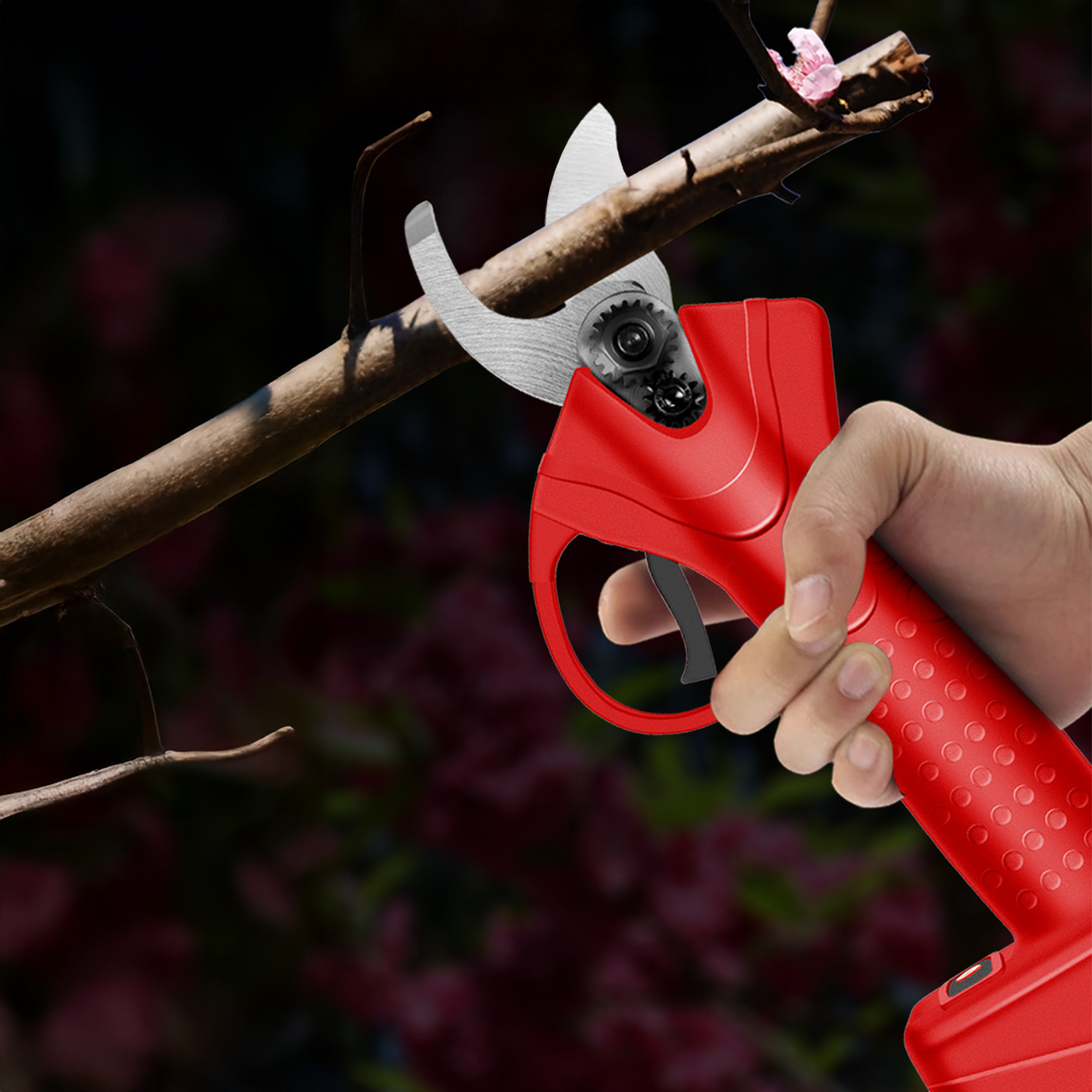Eine Hand hält eine rote elektrische Gartenschere, die einen braunen Ast schneidet. Der Hintergrund ist verschwommen mit dunklen und rötlichen Tönen.