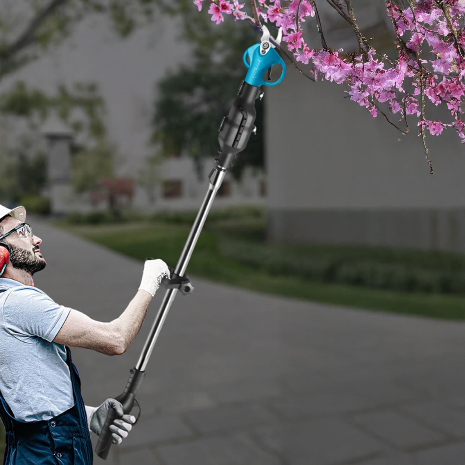 Ein Mann in Overalls schneidet einen blühenden Baum mit einem langstieligen blau-schwarzen Werkzeug. Er trägt eine Schutzbrille und Ohrenschützer.