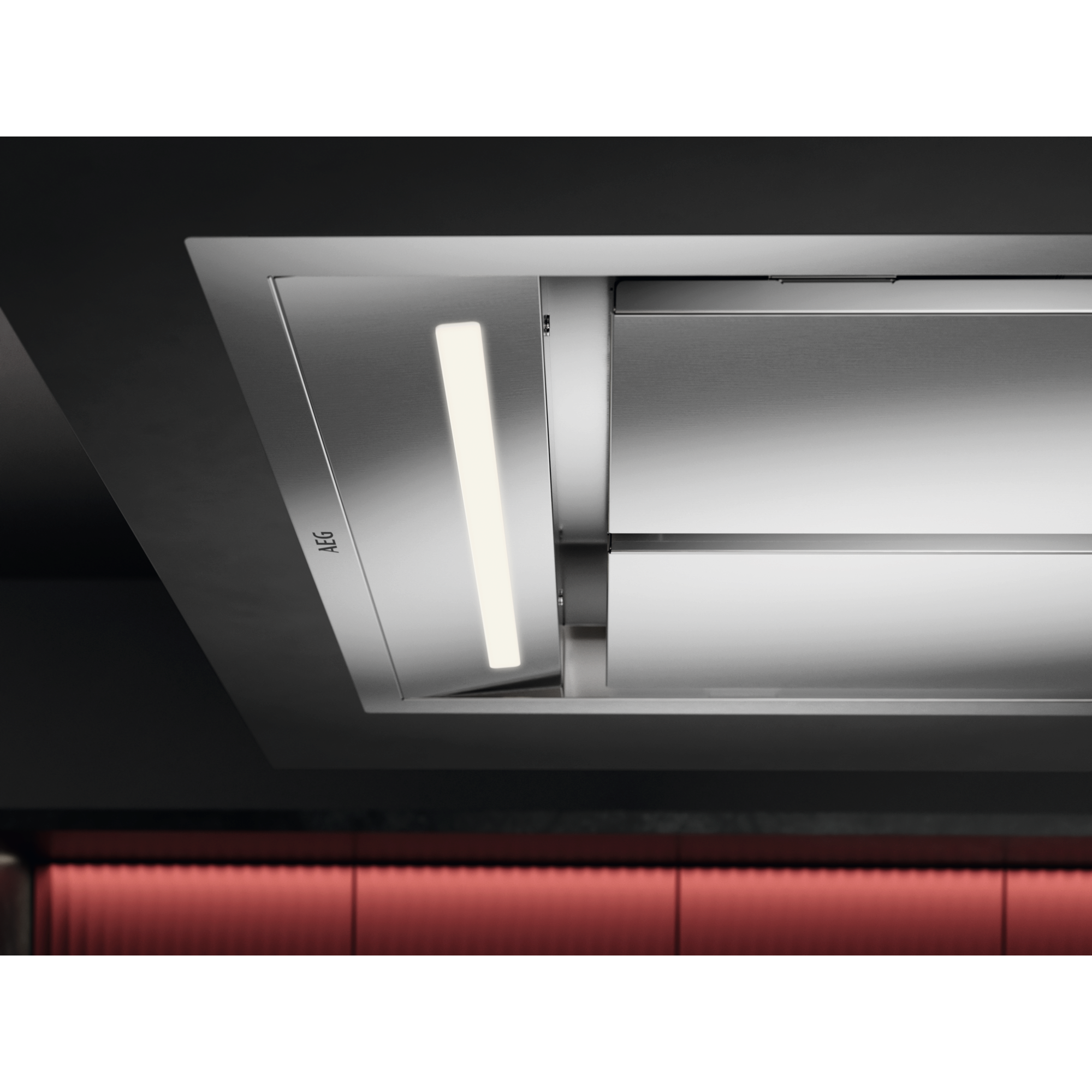 Una cappa in acciaio inossidabile con luce integrata. La cappa ha un logo AEG. Lo sfondo è scuro con illuminazione rossa.