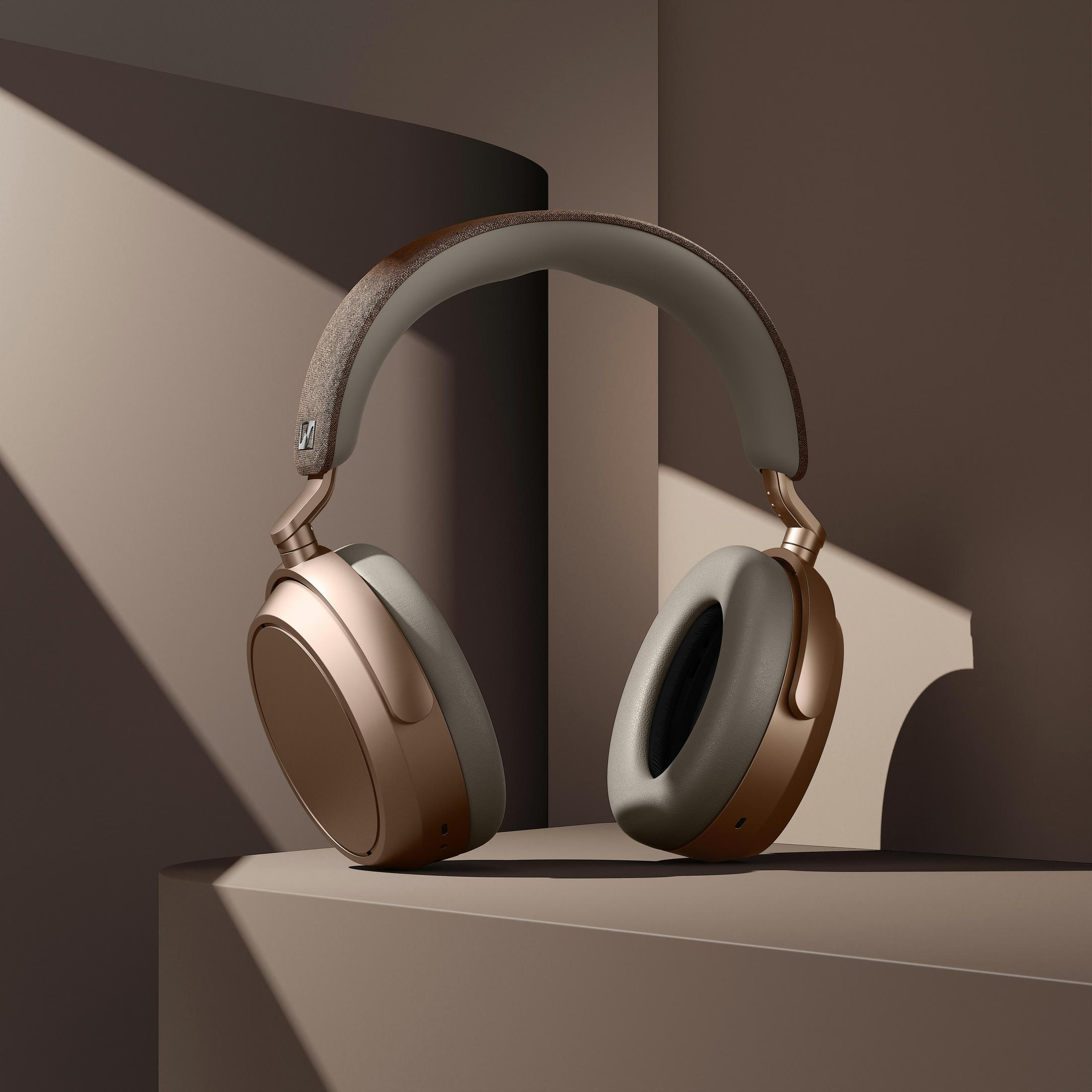 Over-Ear-Kopfhörer in Gold und Grau auf braunem Untergrund. Der Hintergrund zeigt Schatten und Licht.