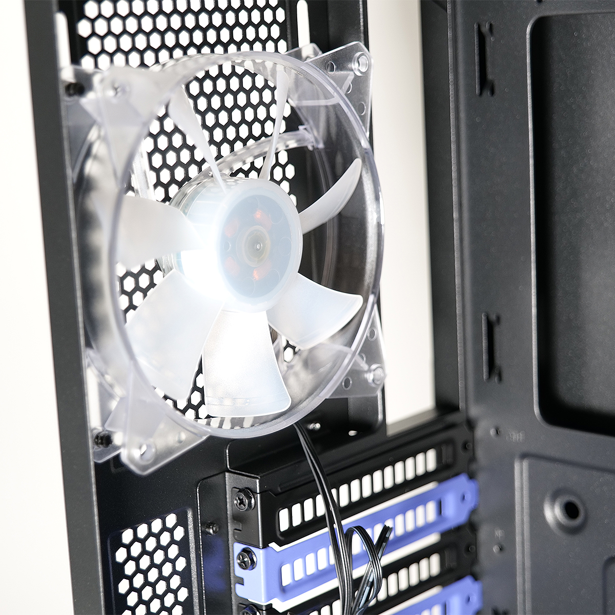 Primo piano dell'interno di un case per computer. È montata una ventola trasparente, con un pannello metallico nero a nido d'ape dietro. Sono visibili alloggiamenti blu per dischi.