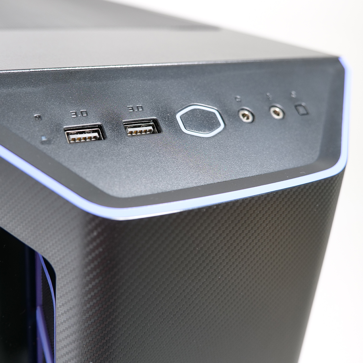 Primo piano di un case di computer. Porte USB, jack audio e pulsante di accensione visibili. Il case ha una texture in fibra di carbonio.