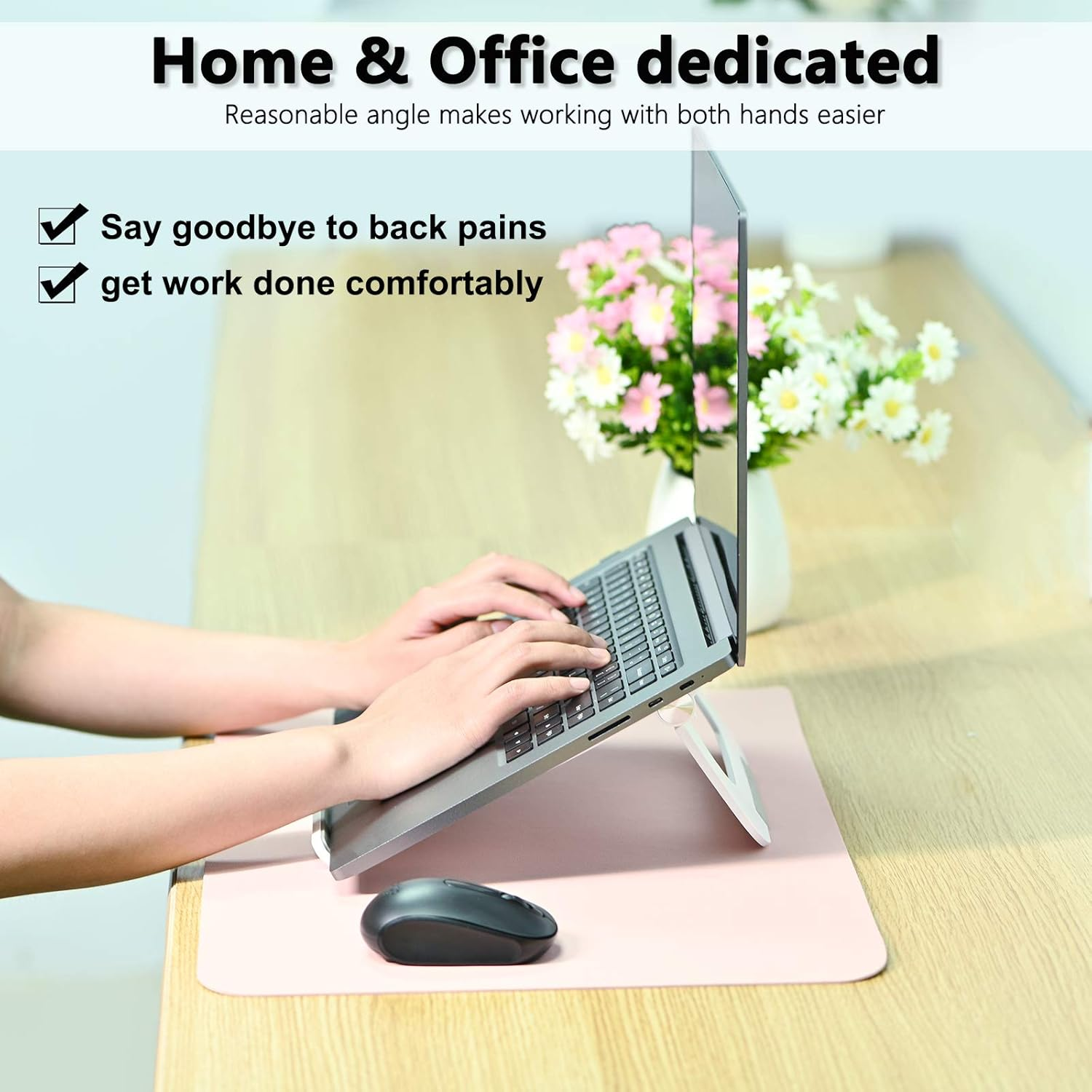 Eine Person tippt auf einem Laptop auf einem Schreibtisch. Eine Maus und ein rosa Pad sind vorne. Blumen sind im Hintergrund.