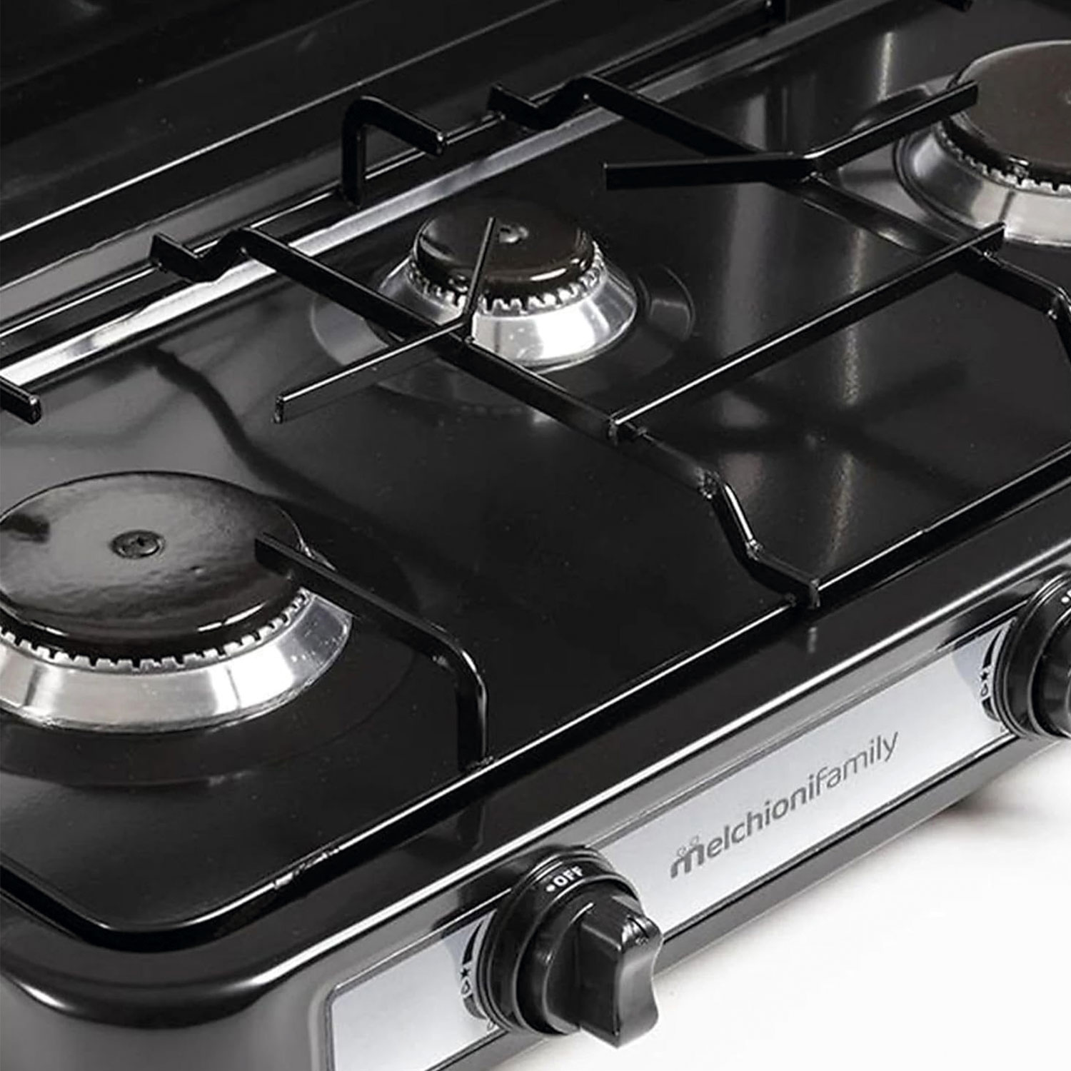 Primer plano de una estufa de gas negra con quemadores plateados y perillas de control. Visible el nombre de la marca melchionifamily.