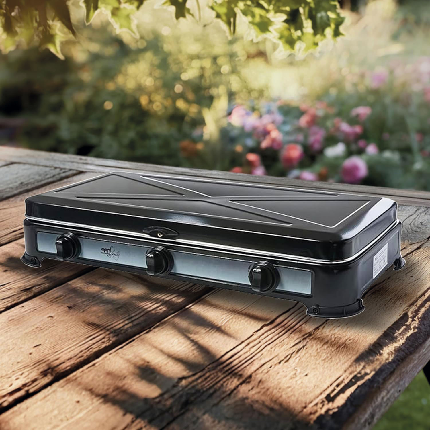 Una estufa portátil negra sobre una mesa de madera. El fondo muestra un jardín borroso con flores y vegetación.