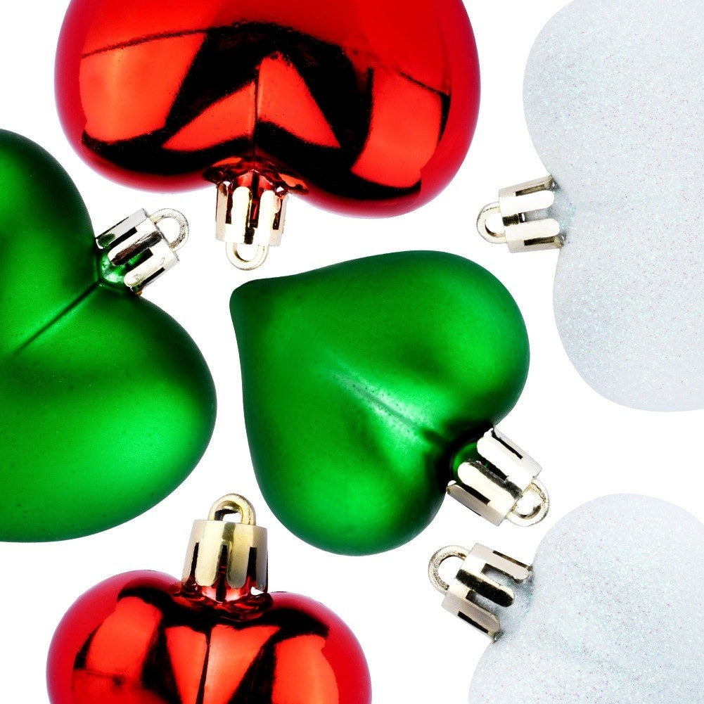 Adornos navideños en forma de corazón rojos, verdes y blancos, con tapas metálicas, sobre un fondo blanco.