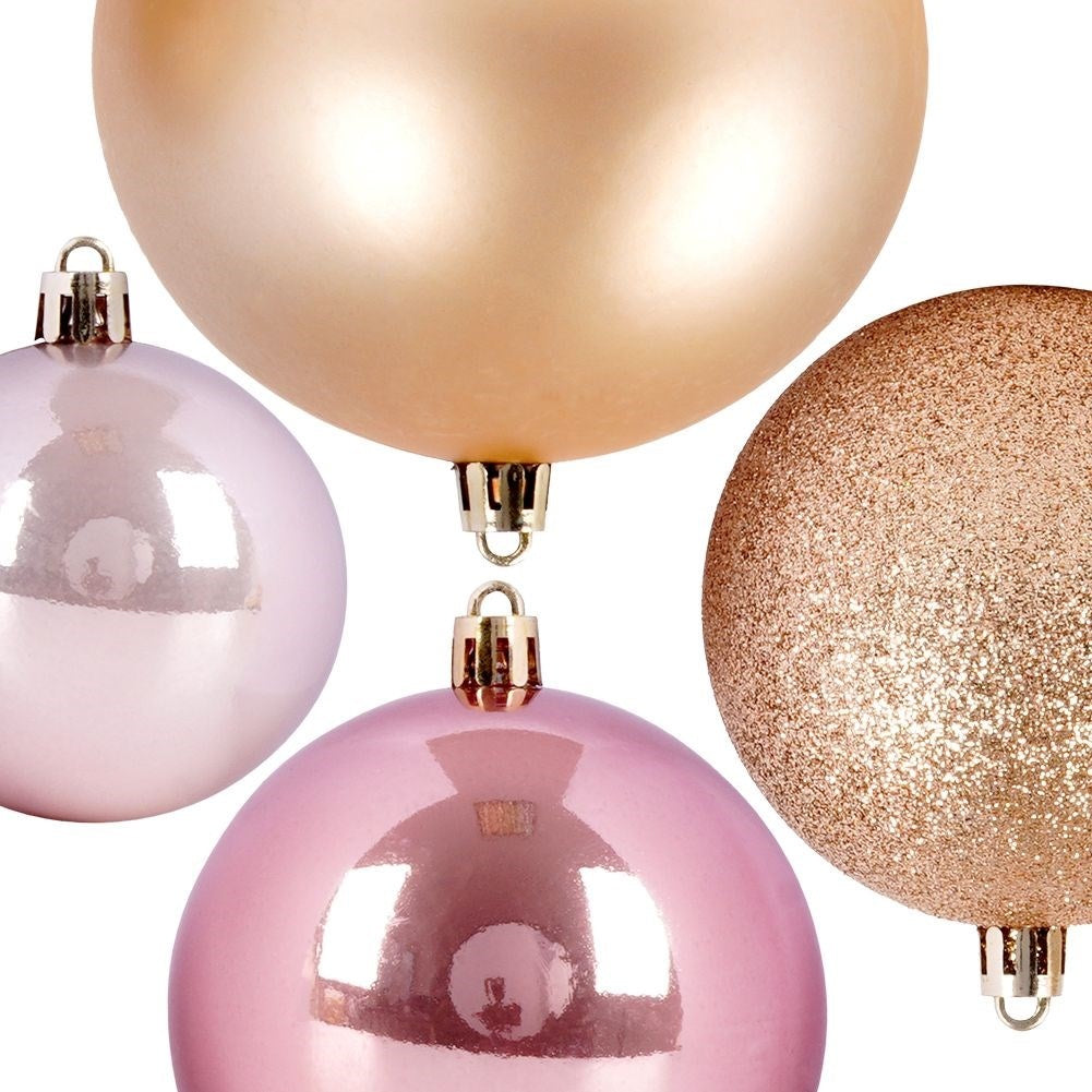Cuatro adornos navideños: oro, rosa, oro rosa y oro con purpurina. Cada uno tiene una tapa y un gancho plateados, sobre un fondo blanco.