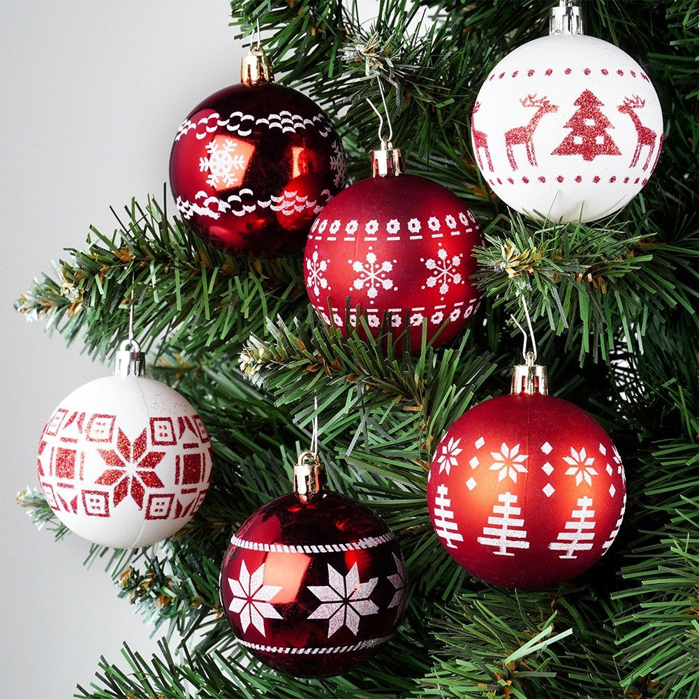 Primer plano de un árbol de Navidad con seis adornos. Bolas rojas y blancas con diseños de copos de nieve y árboles colgando.