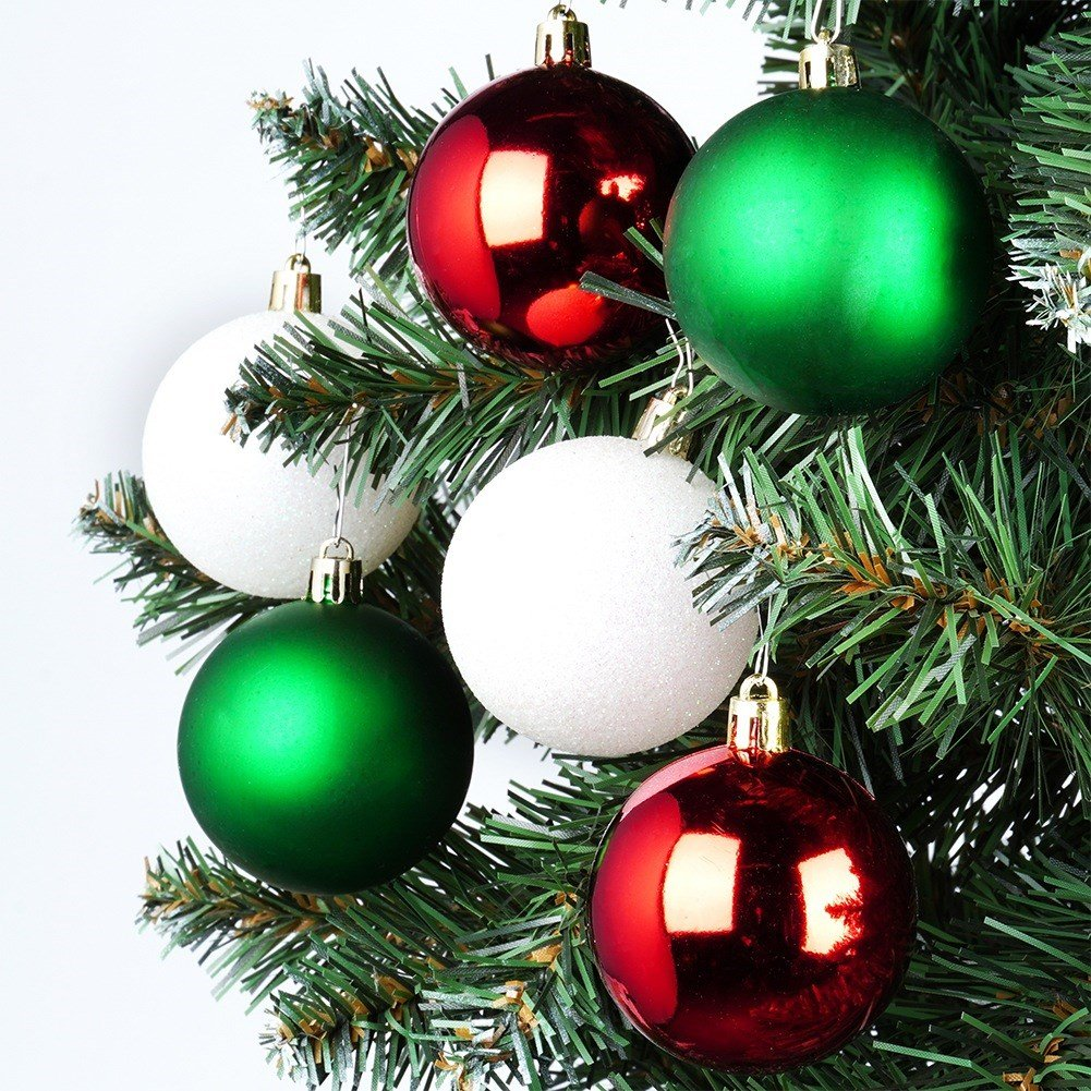 Primer plano de un árbol de Navidad con seis adornos. Los adornos son rojos, verdes y blancos. Ramas de árbol verdes. Fondo blanco.