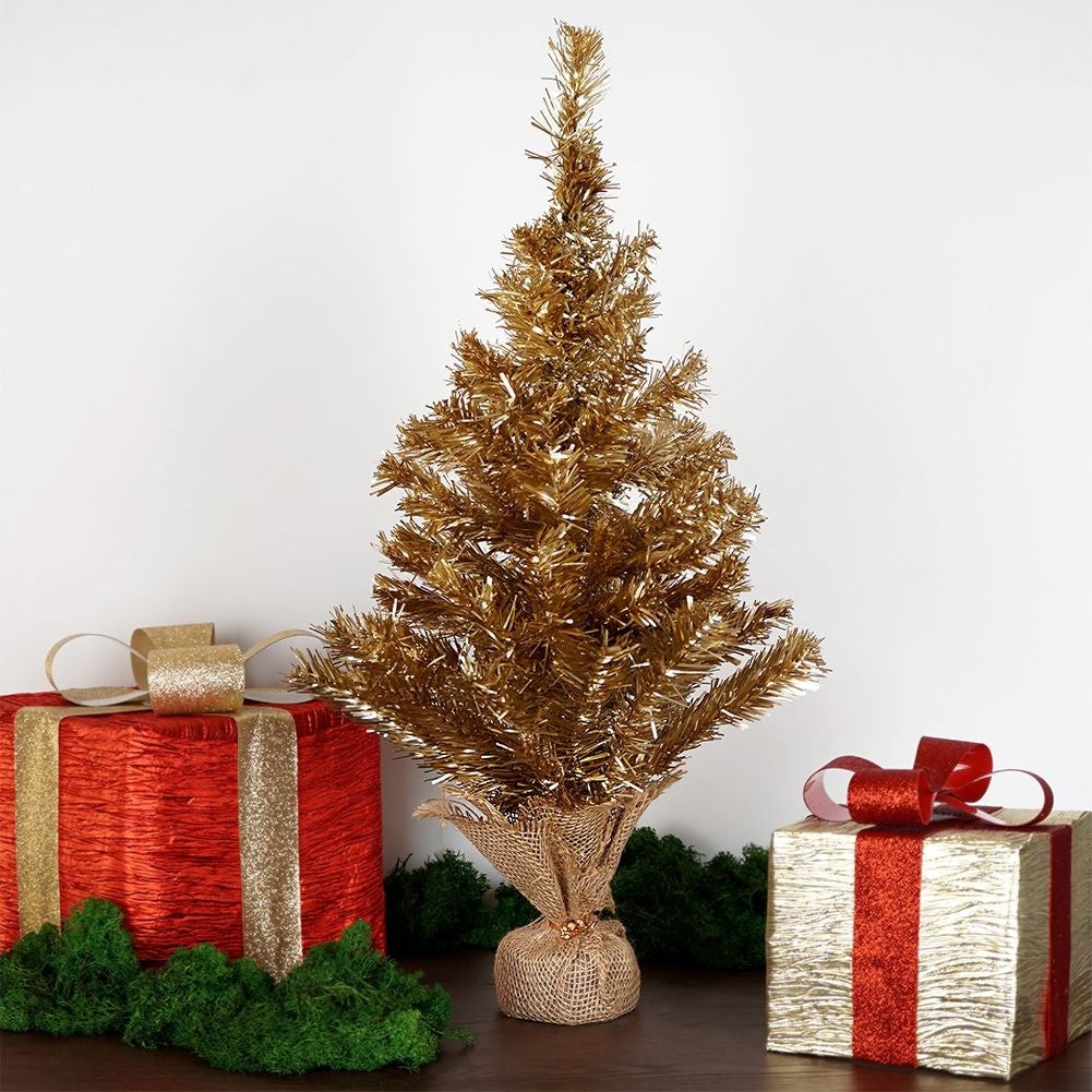 Un árbol de Navidad dorado está entre dos regalos envueltos. Uno es rojo, el otro dorado. Musgo verde en la base.