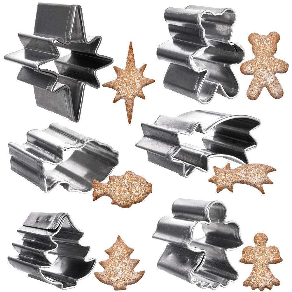 La imagen muestra cortadores de galletas junto a galletas horneadas. Las formas incluyen estrellas, osos, peces, un árbol de Navidad y un ángel. Todo sobre fondo blanco.