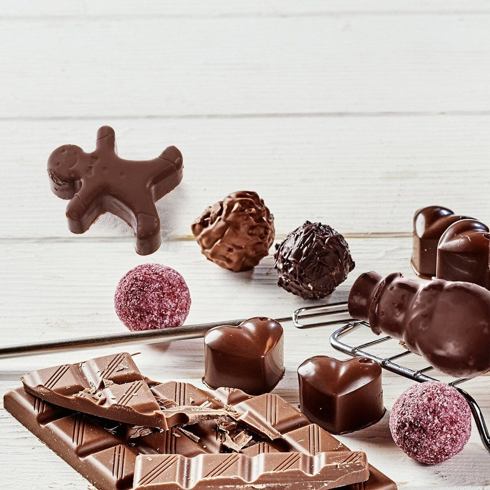 Surtido de chocolates sobre una superficie de madera blanca. Incluye una barra de chocolate, trufas, formas de corazón y un hombre de jengibre.