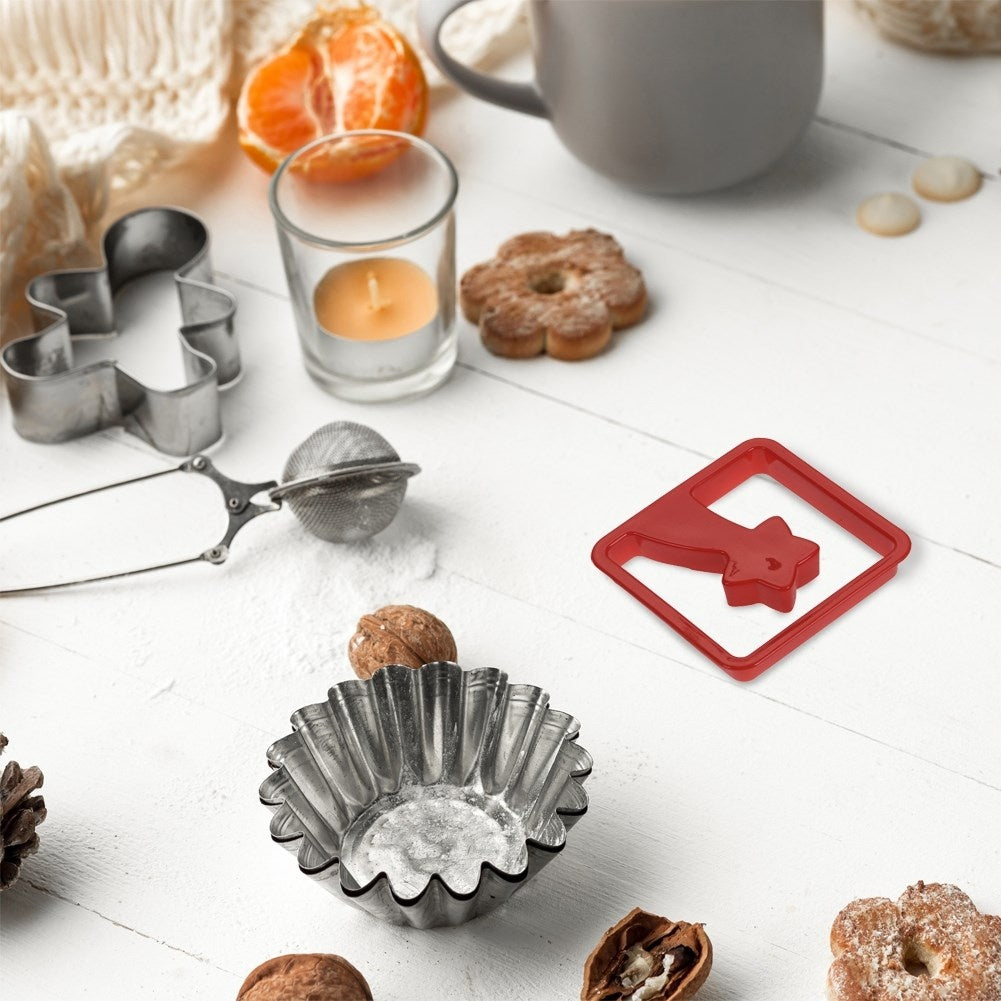 Naturaleza muerta de artículos de repostería sobre una superficie de madera blanca. Incluye cortadores de galletas, nueces, vela, colador de té y una taza.