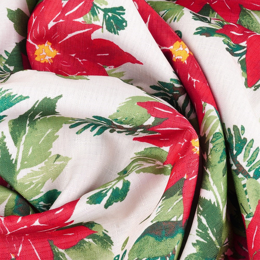 Tela con flores de pascua rojas, hojas verdes y centros amarillos sobre fondo crema. La tela está doblada.