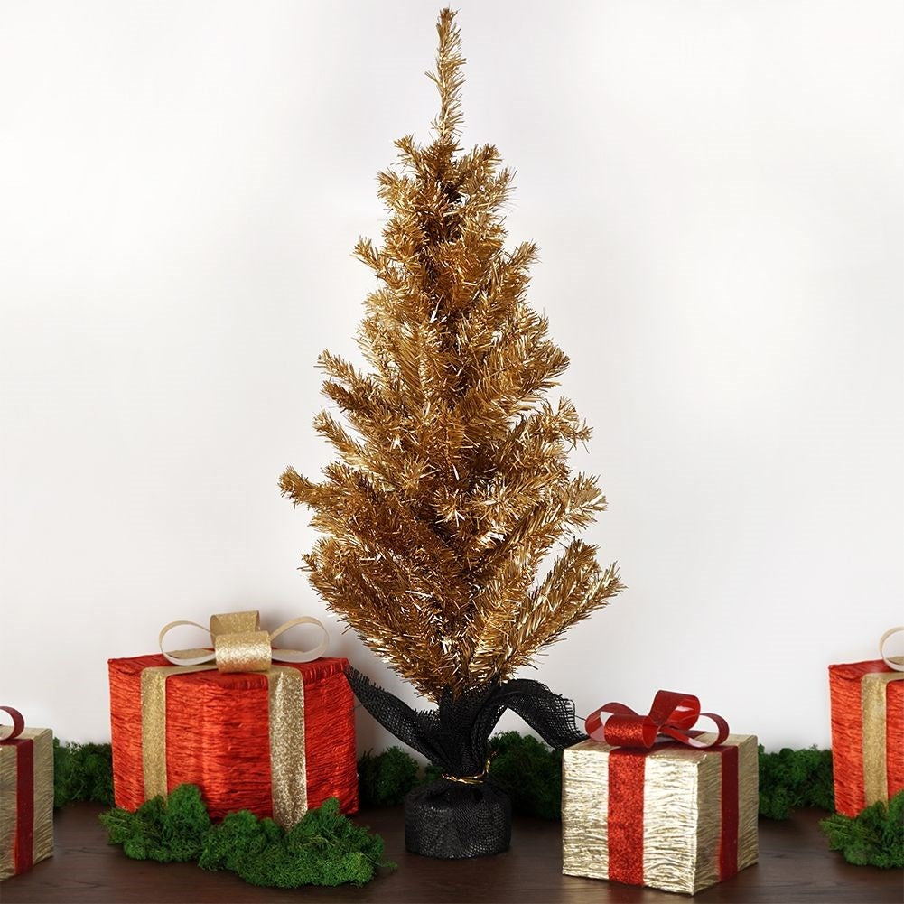 Un árbol de Navidad dorado con cajas de regalo rojas, lazos y musgo verde sobre madera. Fondo de pared blanca.