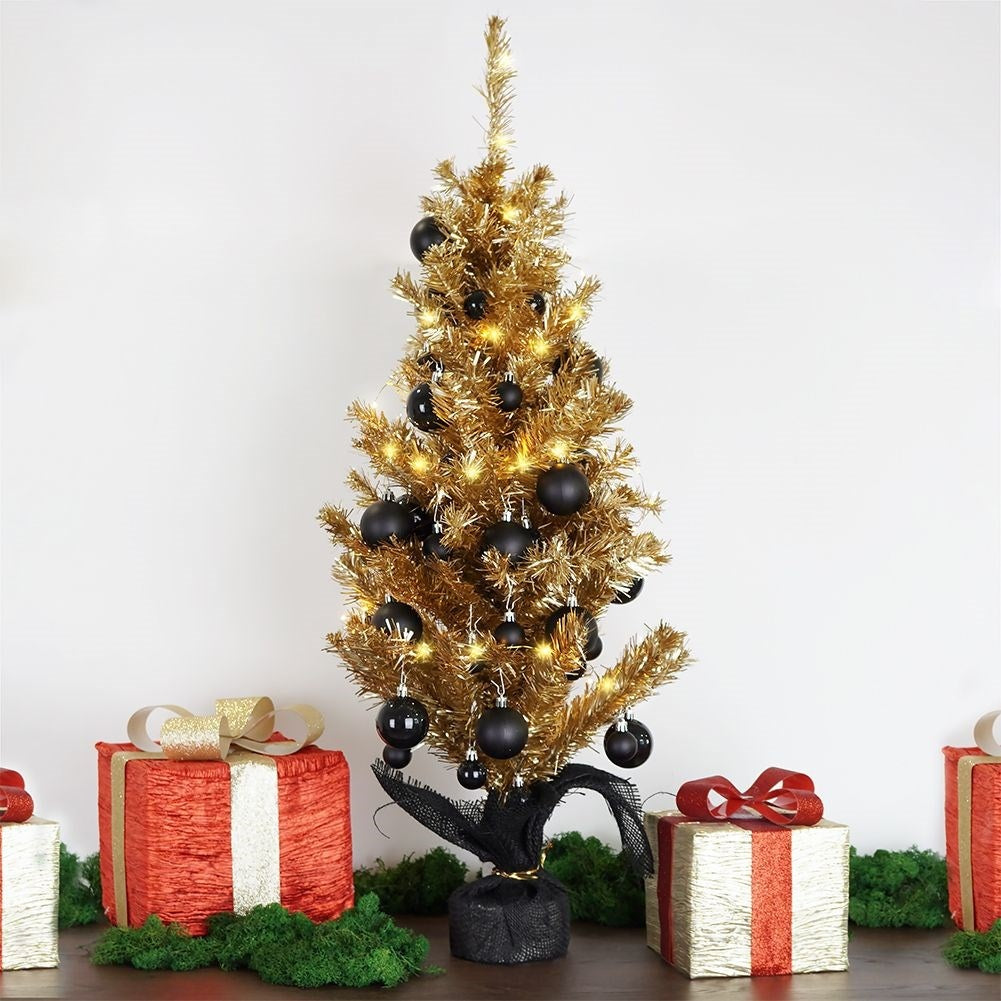 Un árbol de Navidad dorado con adornos negros y luces, rodeado de regalos envueltos en rojo y oro, sobre una superficie de madera.