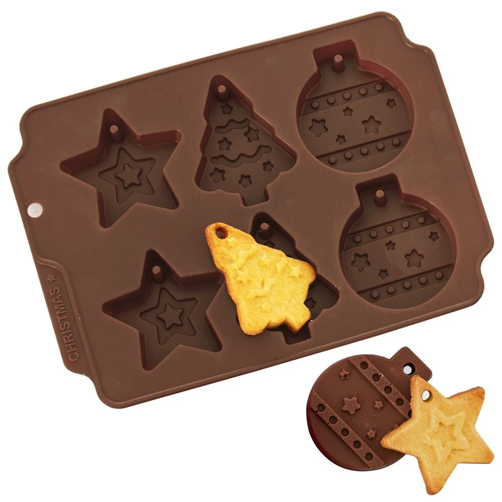 Moldes de galletas marrones con forma de Navidad con una galleta horneada dentro. Una galleta en forma de estrella y adorno está junto al molde.