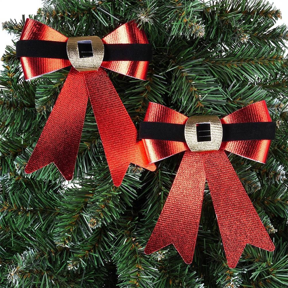 Dos lazos navideños con cintas rojas, bandas negras y hebillas doradas, en un árbol de Navidad verde.