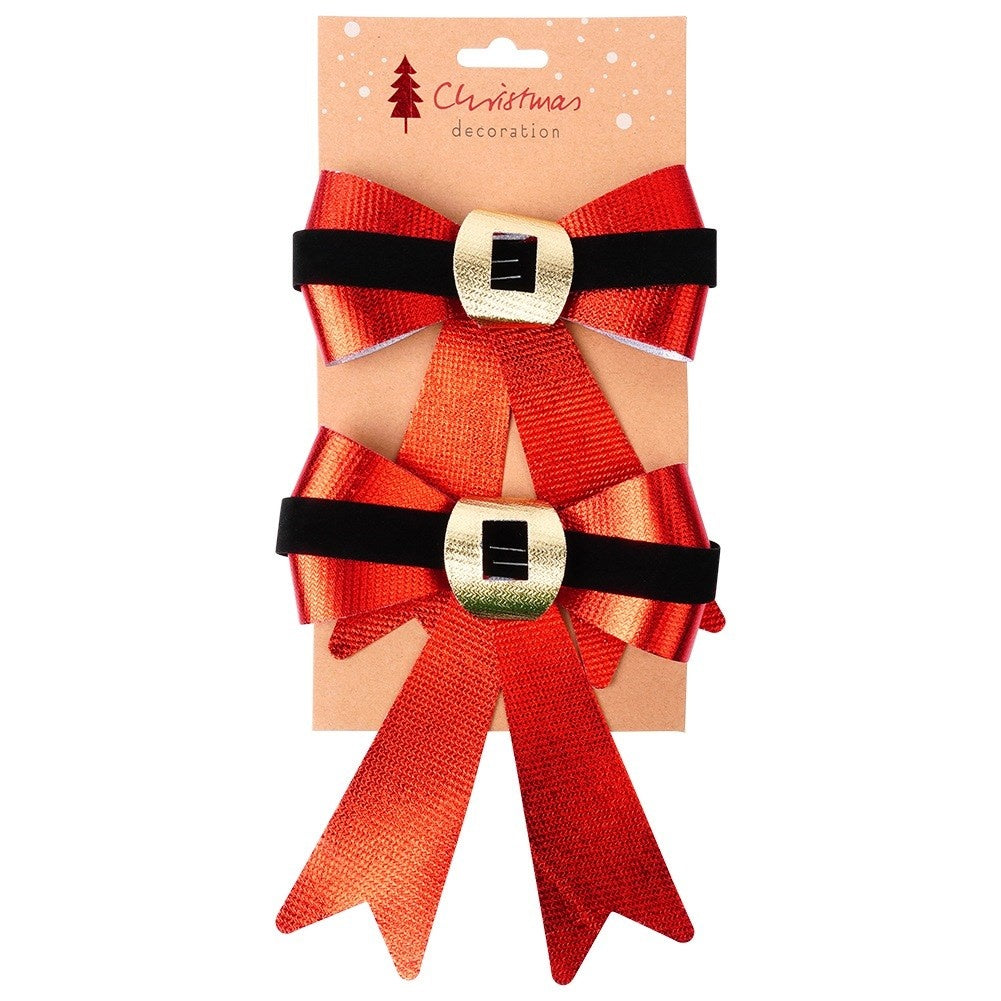 Dos lazos rojos de Navidad con bandas negras y hebillas doradas sobre cartón, etiquetados como 'Decoración navideña'.