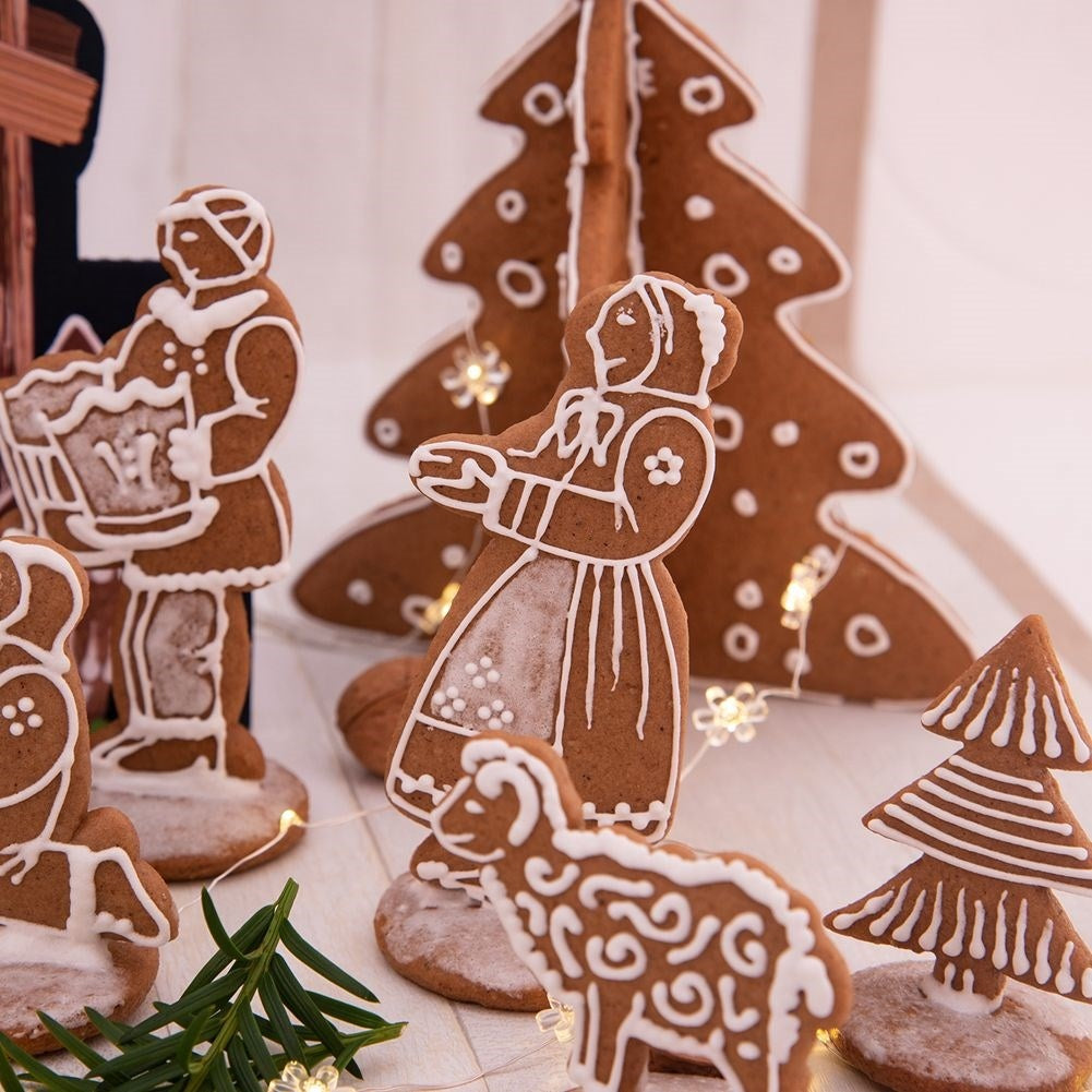 Figuras de pan de jengibre que representan una escena. Las figuras incluyen personas, un árbol y un cordero, todos decorados con glaseado blanco.
