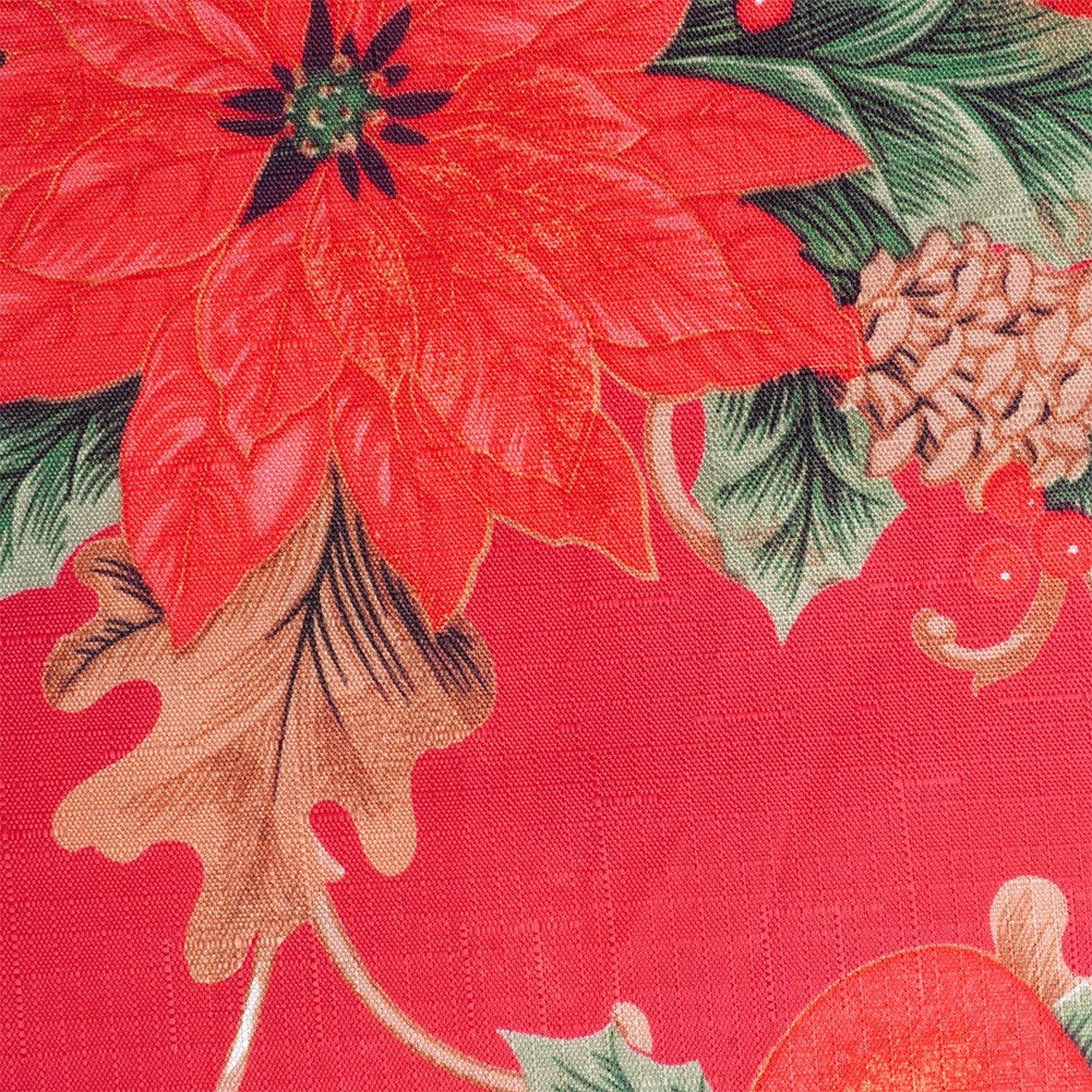 Primer plano de una flor de Nochebuena roja con hojas verdes sobre un fondo de tela roja. También son visibles piñas y bayas.