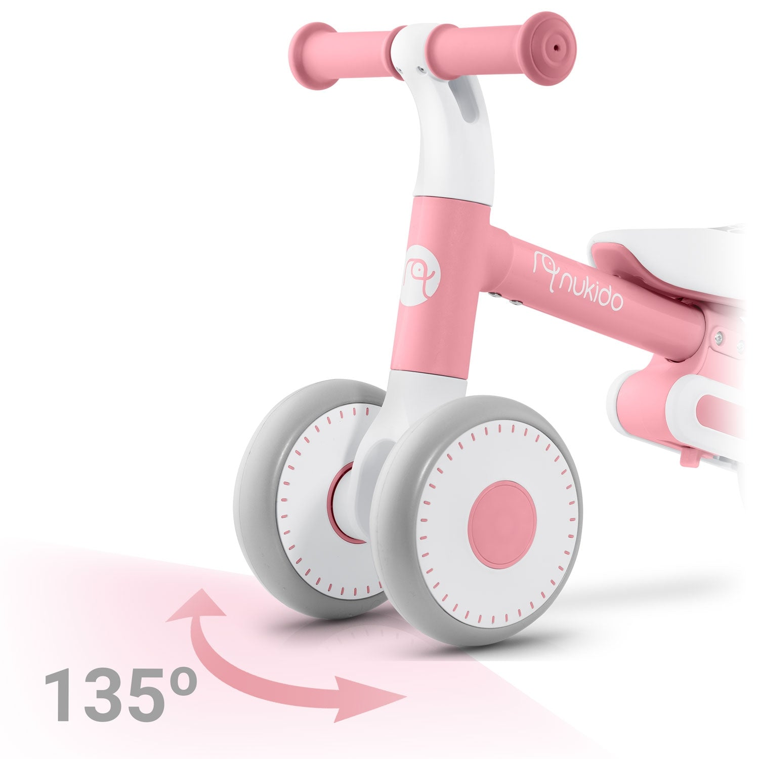 Una bicicleta de equilibrio rosa y blanca con ruedas grises. El ángulo es de 135 grados, ilustrado por una flecha. Marca 'nukido' visible.