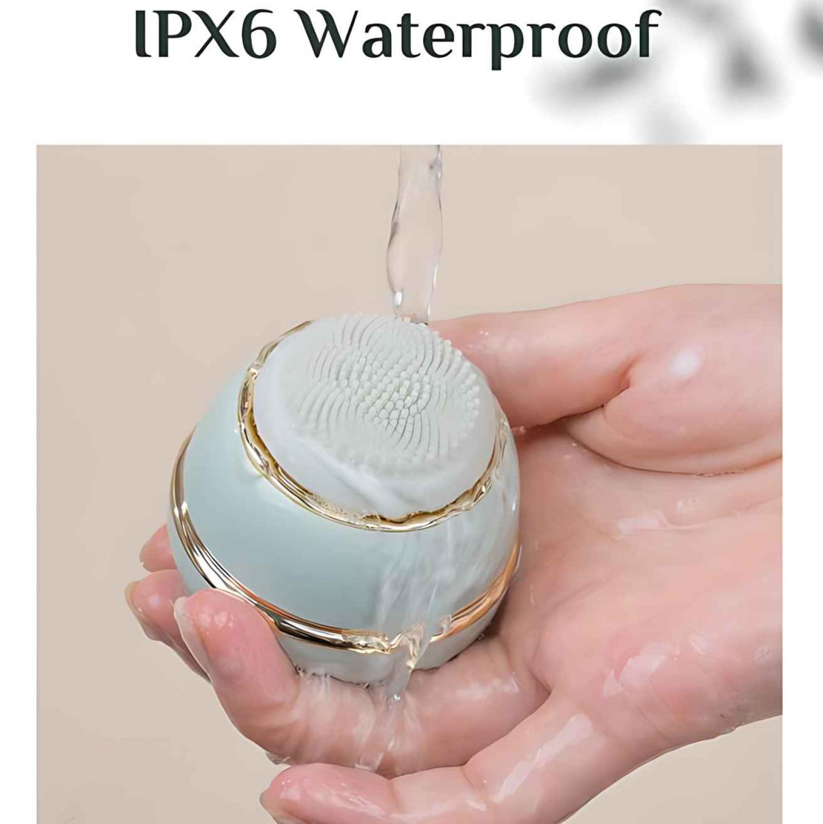Eine Hand hält eine teal-goldfarbene Gesichtsreinigungsbürste, Wasser gießt darüber. Der Hintergrund ist neutral.