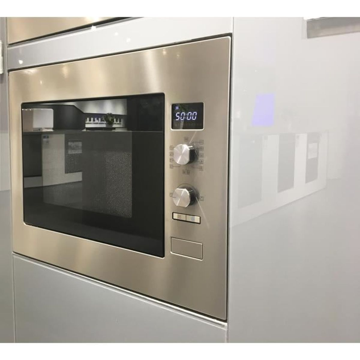 Un horno microondas de acero inoxidable está instalado en un gabinete gris. Se muestra la hora 50:00. Hay perillas y una puerta.