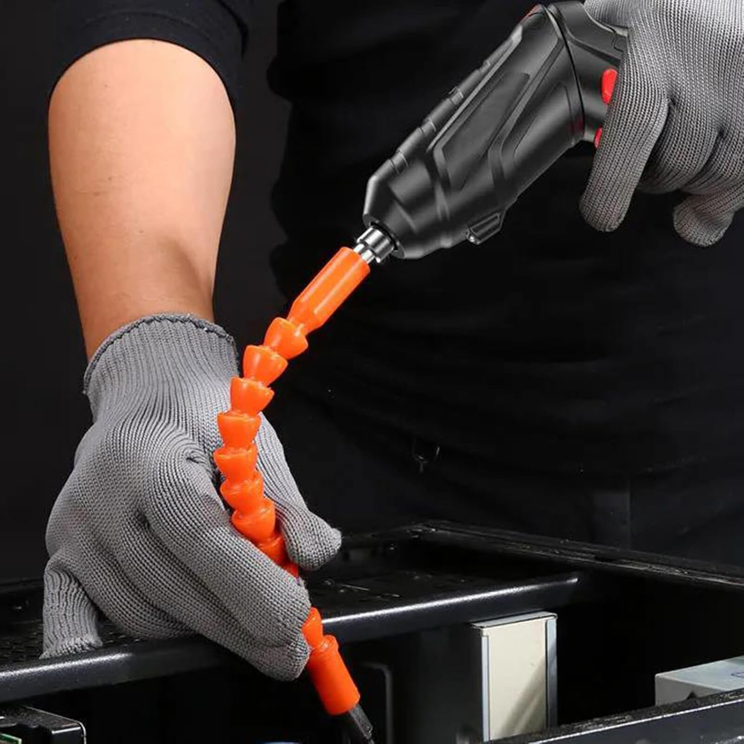 Persona che utilizza un elettroutensile nero con prolunga flessibile arancione, indossa guanti grigi, lavorando su un case di computer nero.