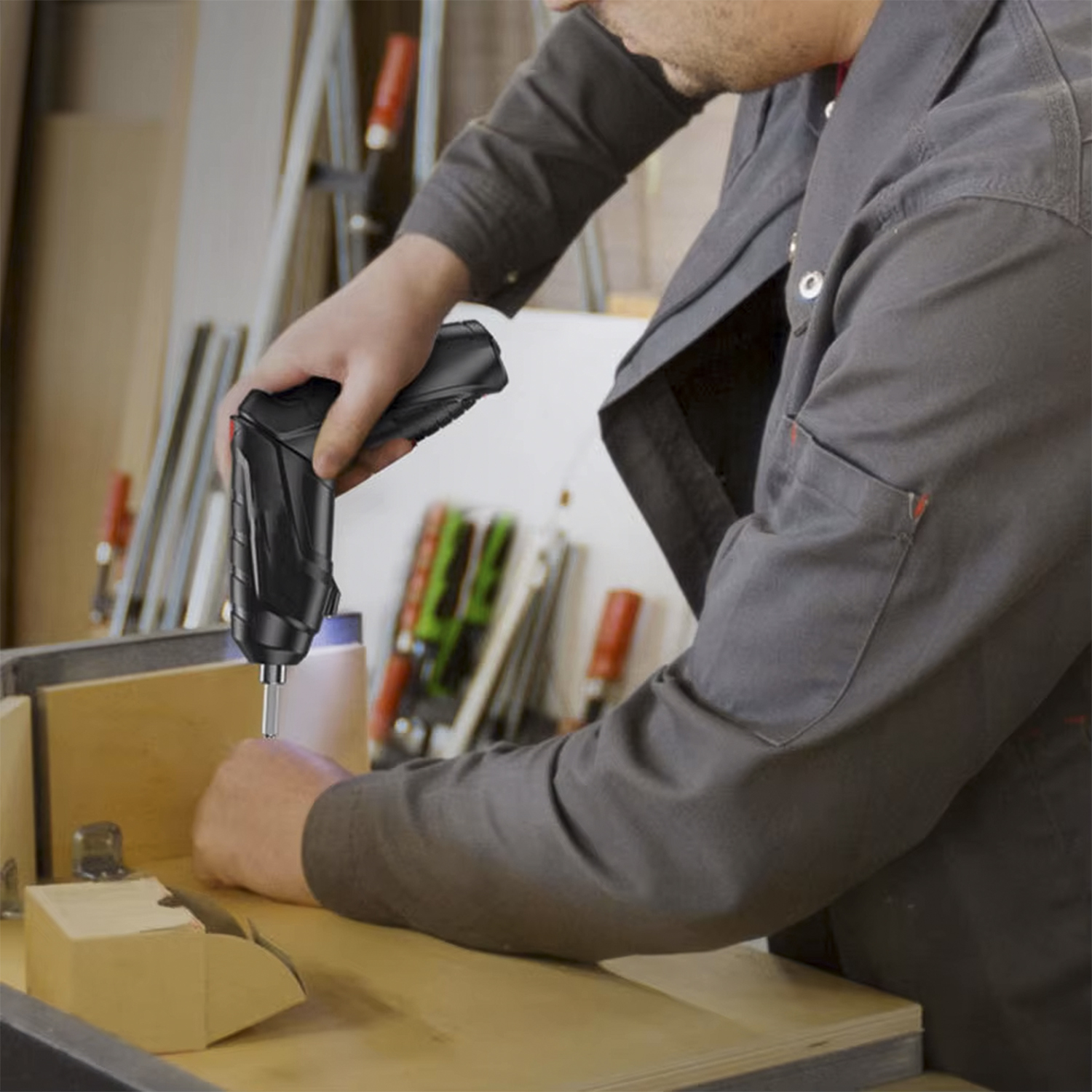 Una persona con una giacca da lavoro grigia utilizza un avvitatore a batteria nero per lavorare a un progetto in legno.