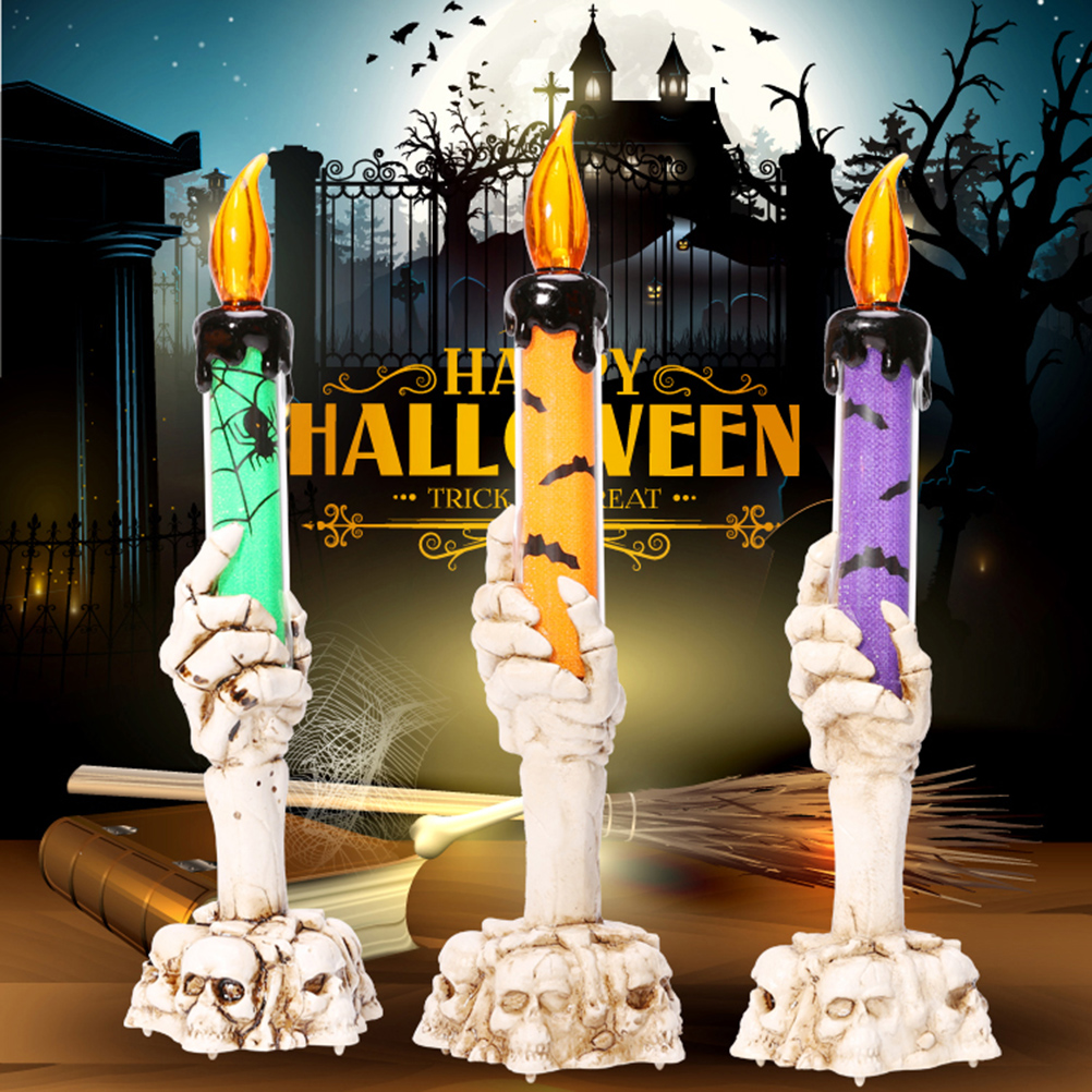 Drei Halloween-Kerzen in Skeletthänden, verschiedene Farben, mit einem gruseligen Hintergrund mit einem Spukhaus und Fledermäusen.