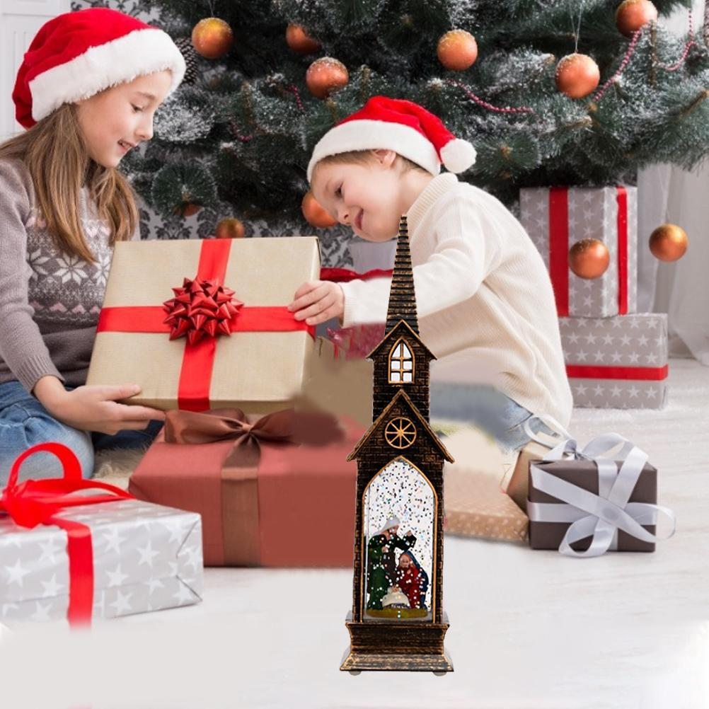 Zwei Kinder mit Weihnachtsmützen öffnen Geschenke am Weihnachtsbaum. Eine kirchenförmige Schneekugel steht im Vordergrund.