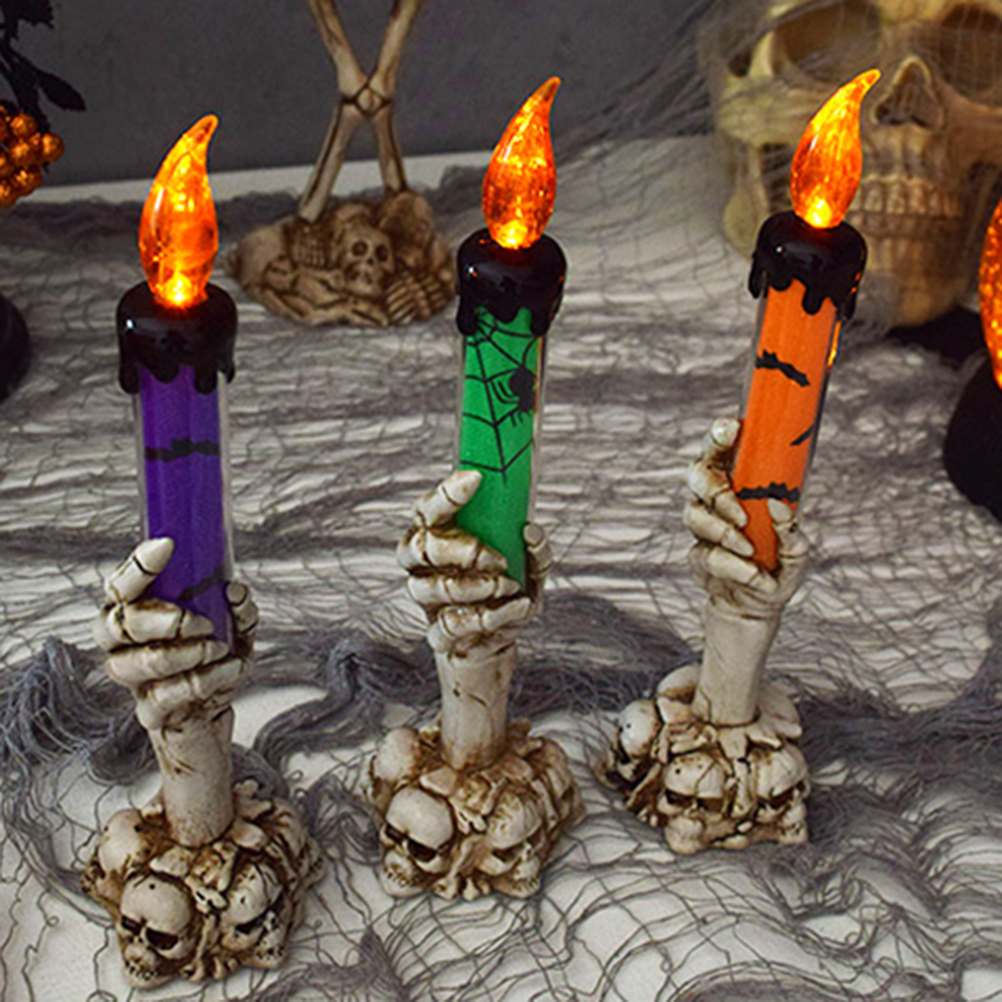 Drei Halloween-Kerzen mit orangefarbenen Flammen. Lila, grüne und orangefarbene Kerzenkörper werden von Skeletthänden auf Schädelbasen gehalten.