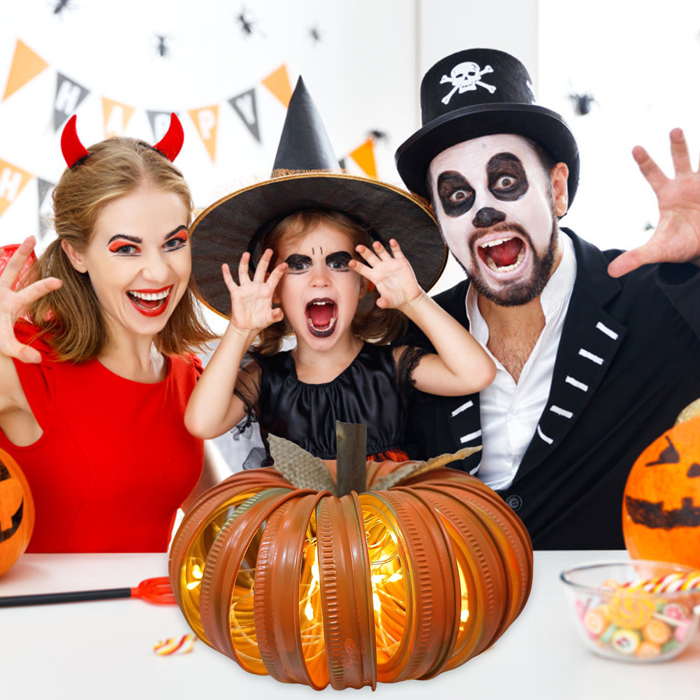 Eine Familie in Halloween-Kostümen. Im Vordergrund eine Kürbisdekoration mit Lichtern. Süßigkeiten und Kürbisse sind ebenfalls zu sehen.