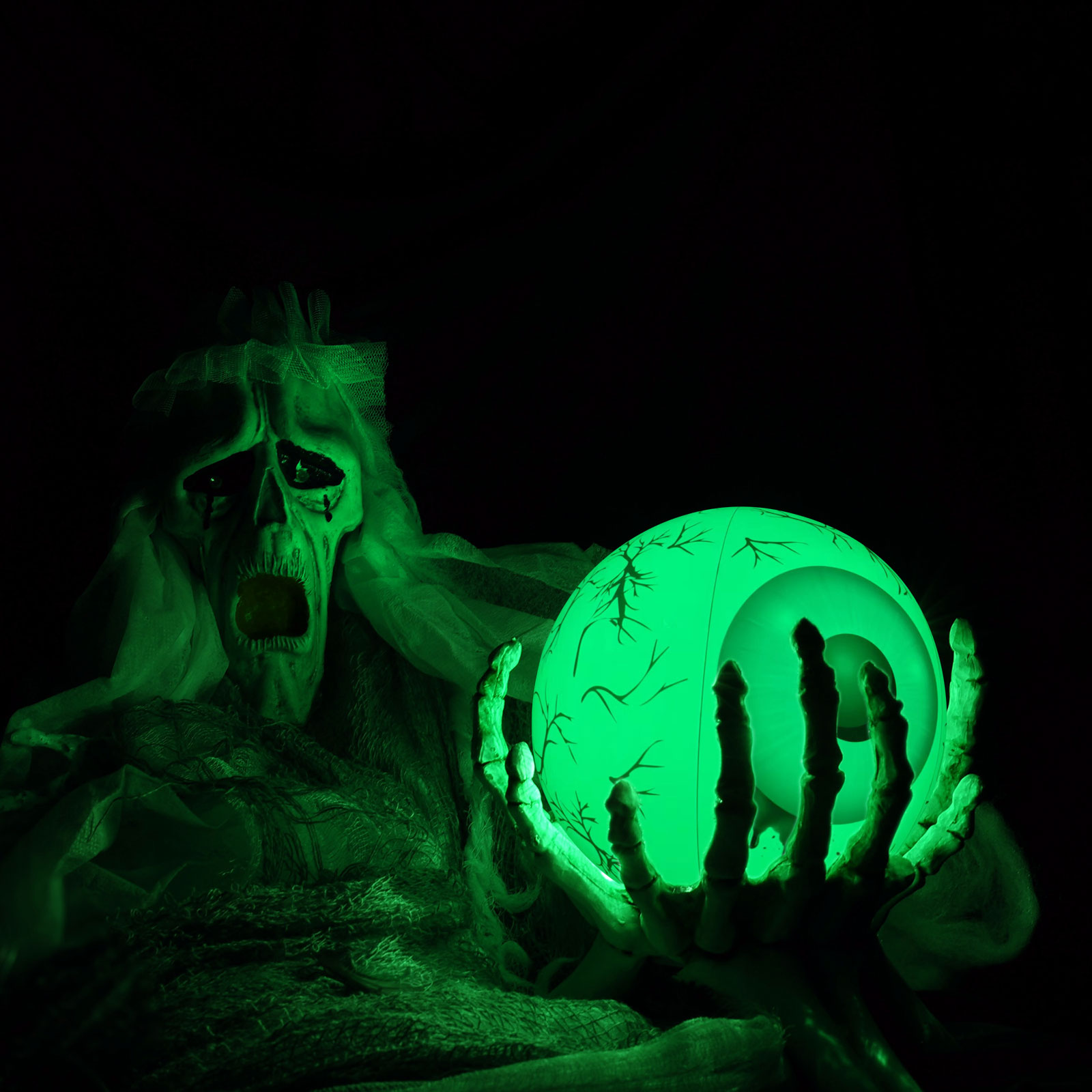 Eine grün beleuchtete Halloween-Figur hält ein leuchtendes Augapfel. Die Figur hat ein skelettartiges Gesicht und Hände, vor schwarzem Hintergrund.