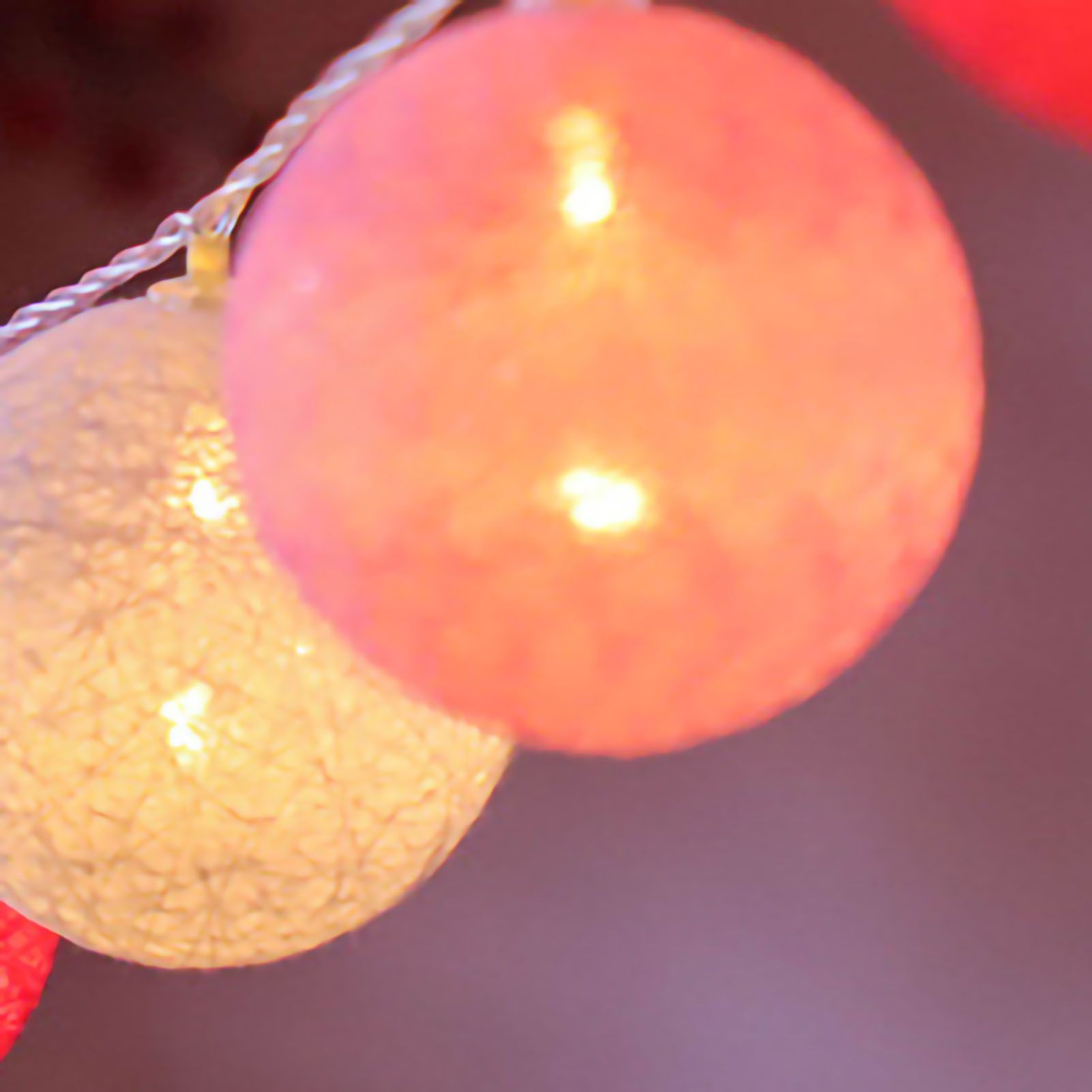 Nahaufnahme von leuchtenden rosa und weißen Lichterketten. Der Hintergrund ist eine verschwommene Mischung aus Lila und Rot.